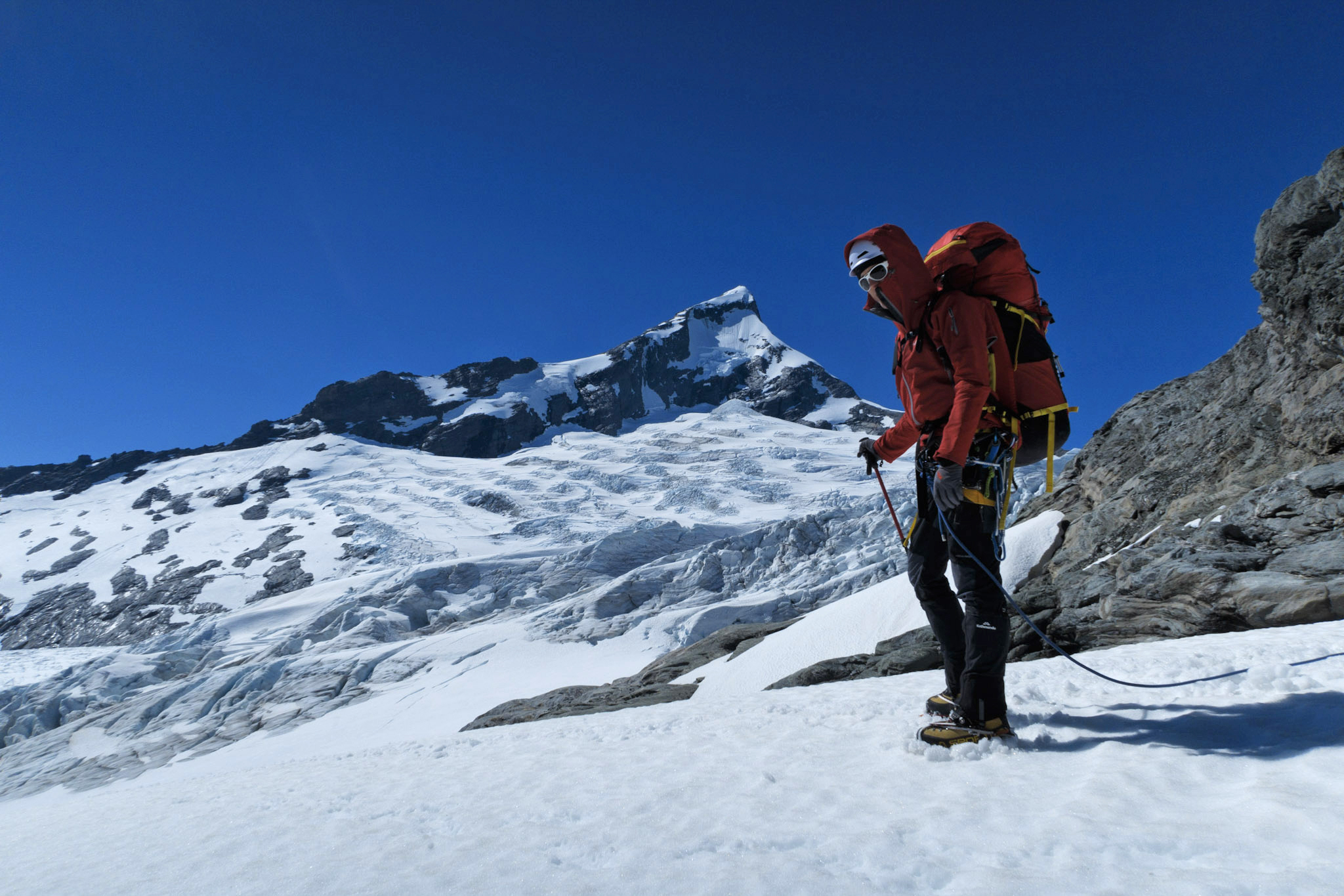 A climber stands in front of the majestic peak Tititea, Mount Aspiring