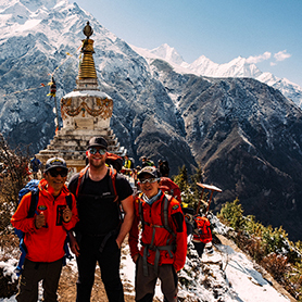 Trekkers stand beneath a stupa enroute to Everest Base Camp, tree clad, snow covered hills behind.