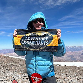 A climber celebrates on the summit of Aconcagua holding an Adventure Consultants flag