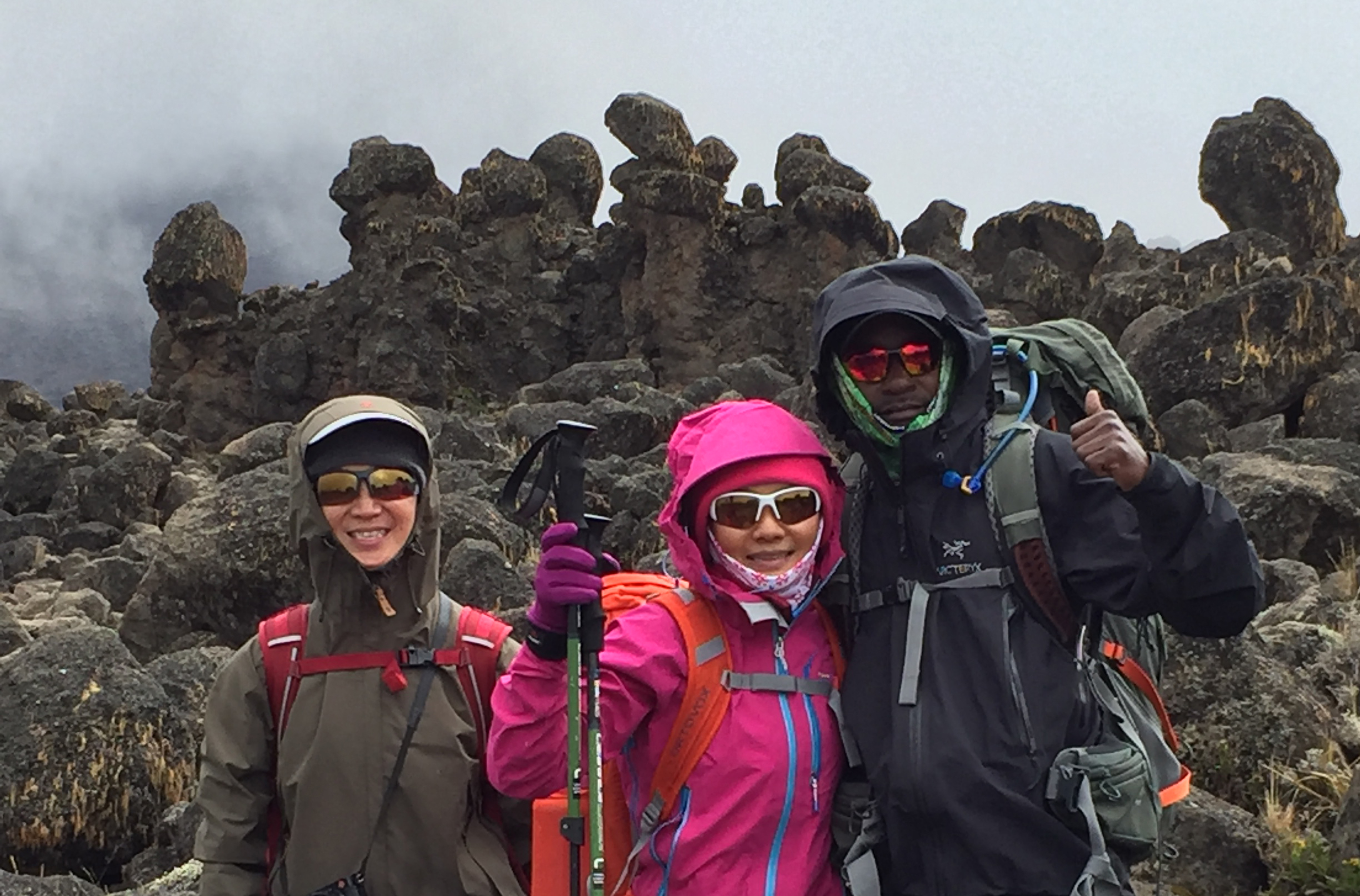 Two climbers with their local guide stand in front of the Lava Tower, an unusual formation of rocks on the slopes of Kilimanjaro.
