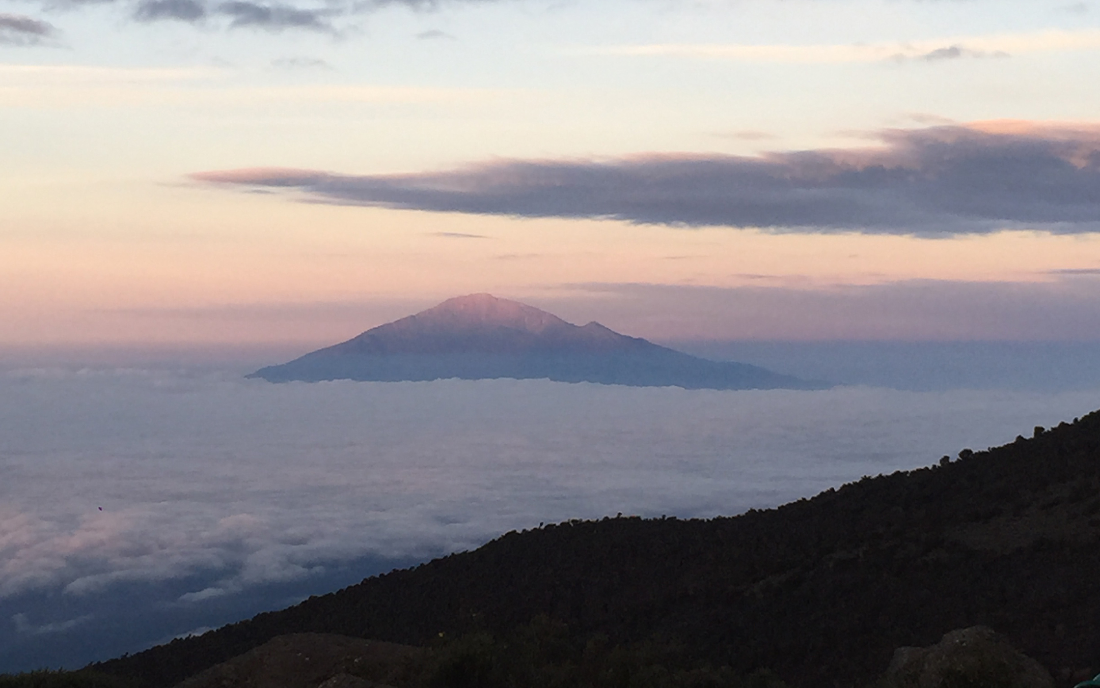 Sunset views across to Mount Meru from Mount Kilimanjaro, the plains below shrouded in a sea of fog.