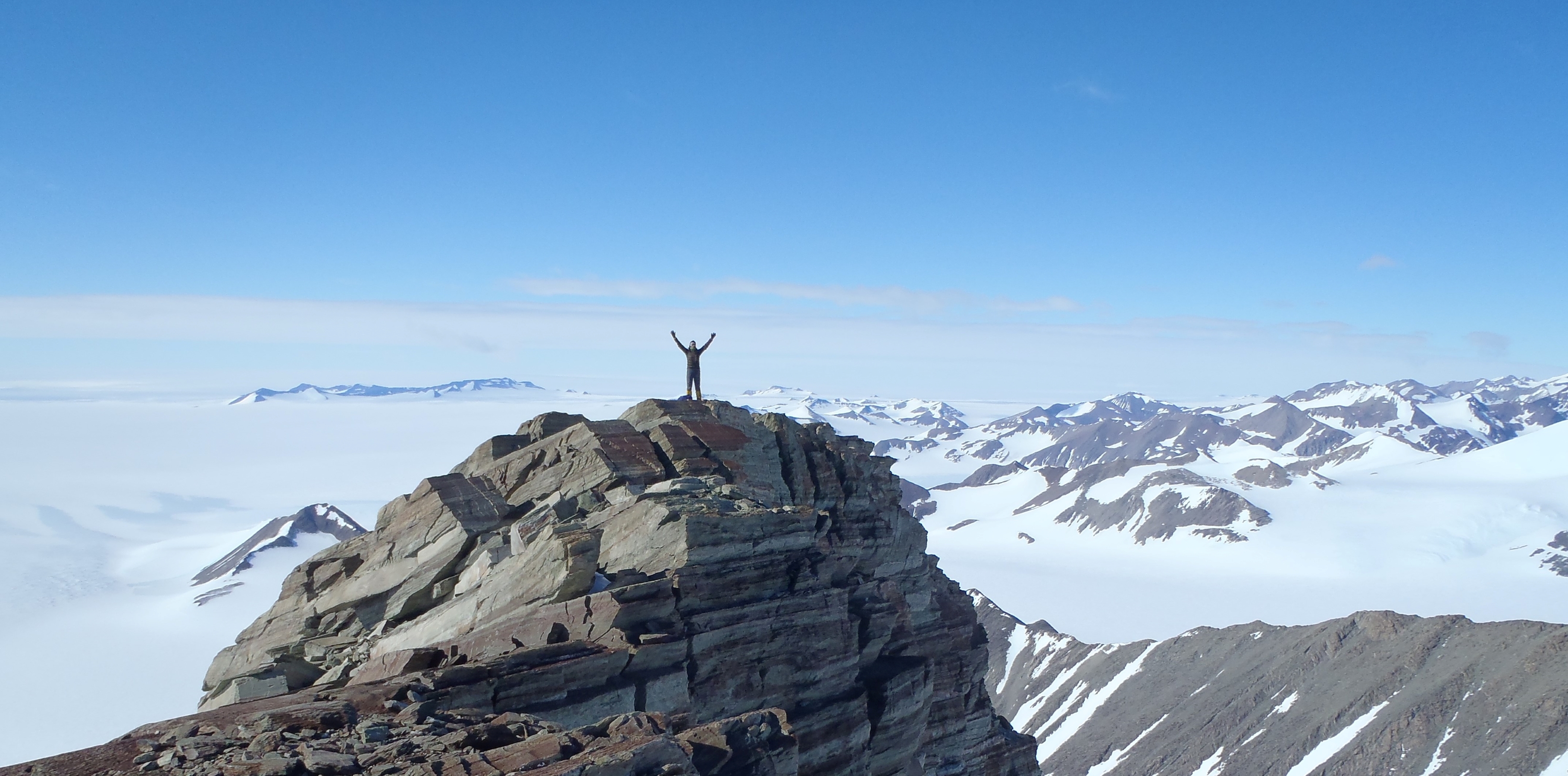 A climber on a rocky summit in Antarctica