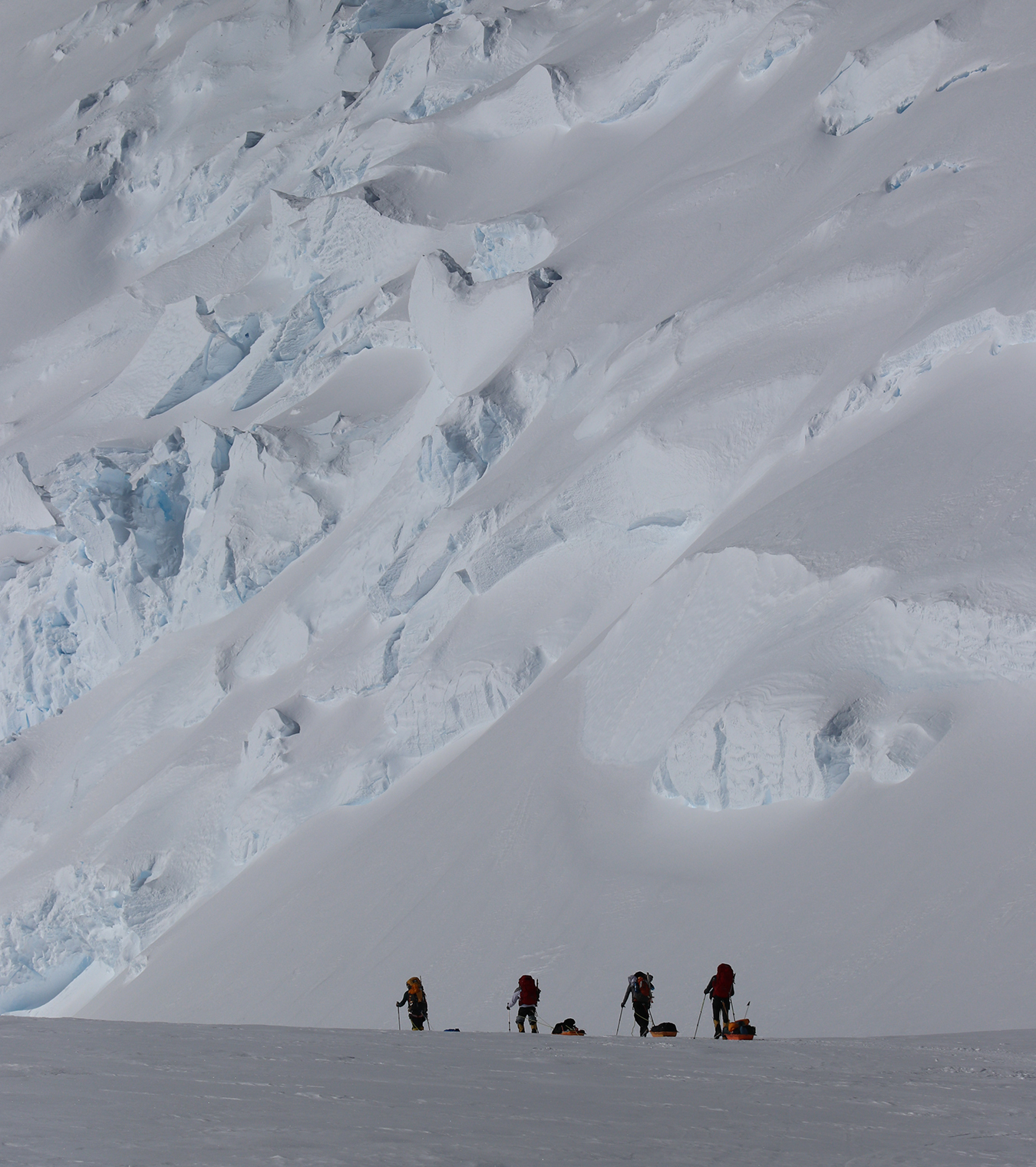 Climbers hauling sleds to Camp 1 dwarfed by the towering ice cliffs of Mount Vinson.