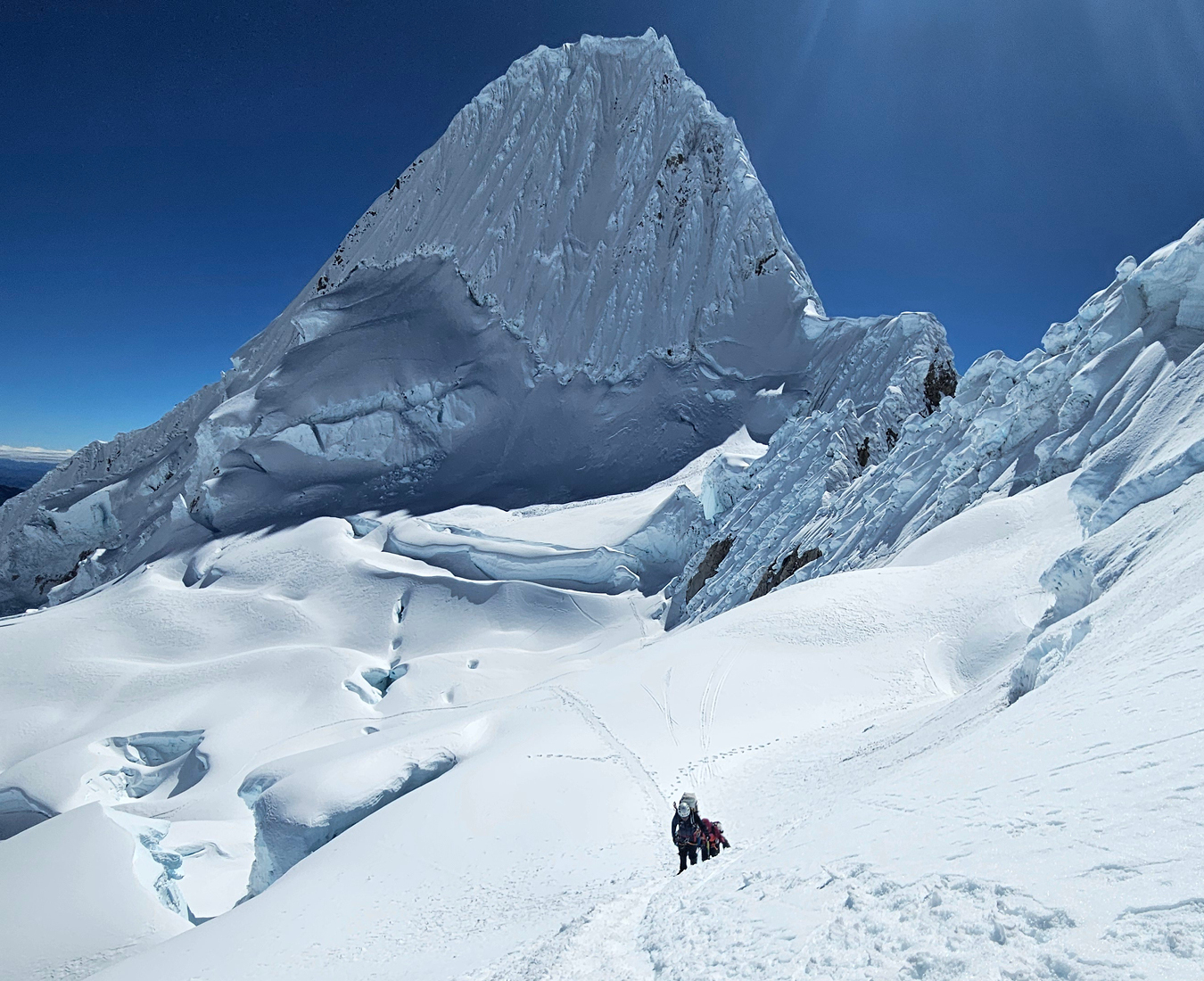 A team return to camp from a successful climb of Alpamayo. Stunning conditions and bright blue sky behind the pyramid shaped peak.