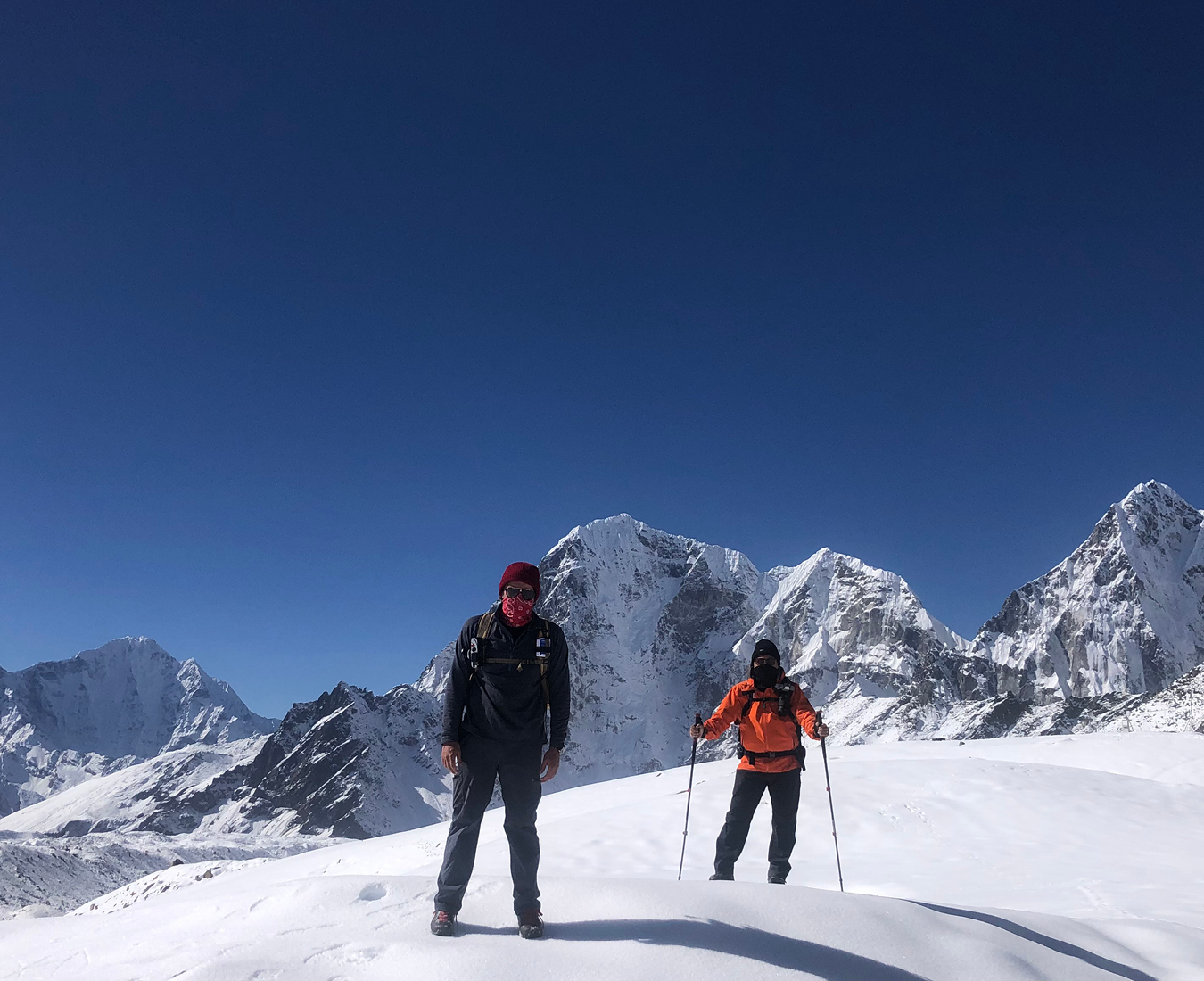 Two trekkers stand in fresh snow above Lobuche village enroute to Everest Base Camp. Bright clear blue skies dominate the horizon with snow capped giant peaks behind.
