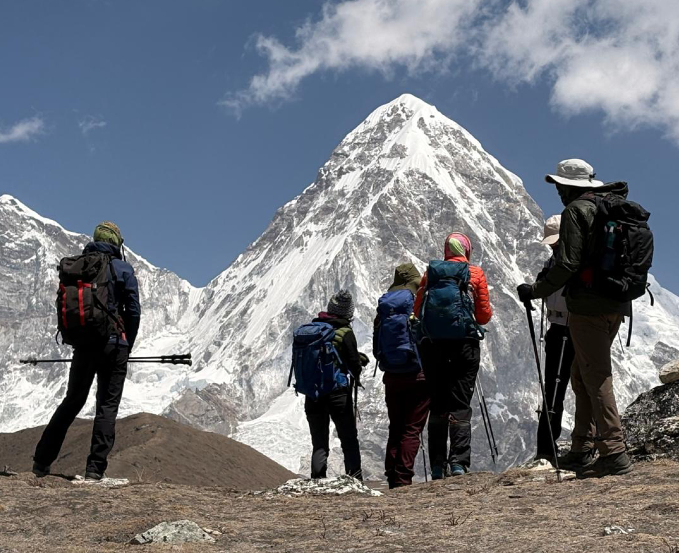 A group of trekkers stand with their backs to the camera taking in the view of Pumori a steep sided pyramid shaped peak near Mount Everest.