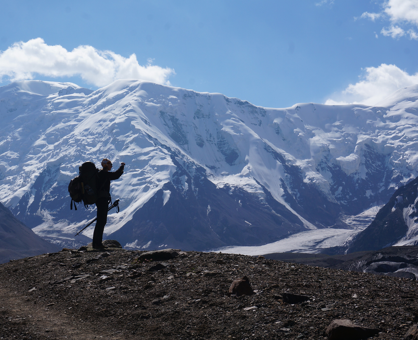 A climber takes a photo silhouetted by the immense Pamir Mountains in the background.