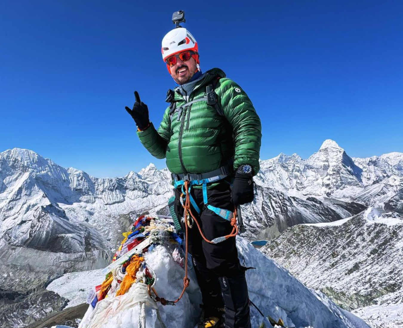 AC climber Wayne Ryan on the summit of Island Peak, Nepal. Stunning mountain vistas and bright blue sky behind.