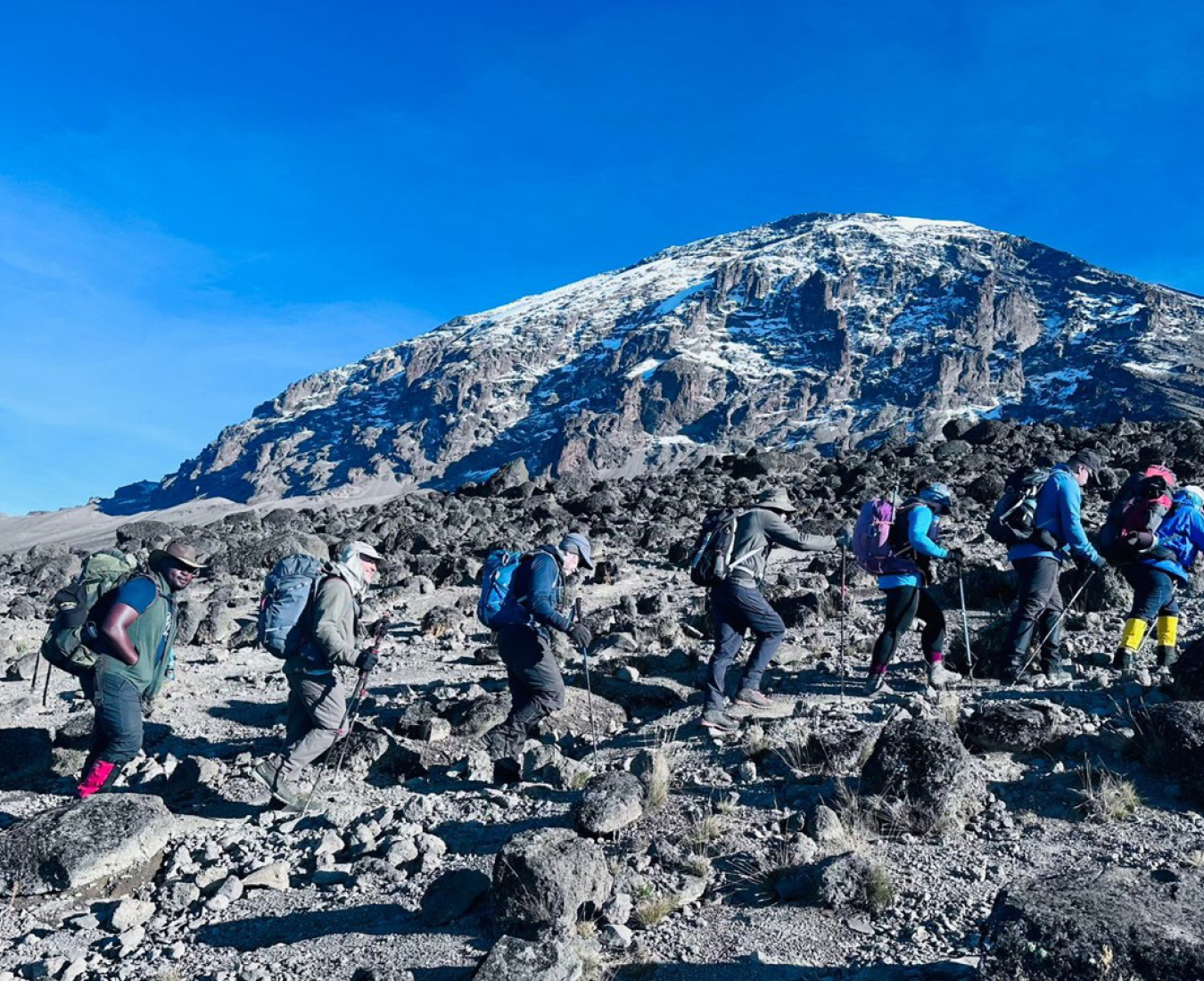 Blue sky and a dusting of fresh snow on the tops of Mount Kilimanjaro as climbers traverse the mountain towards Barafu Camp.