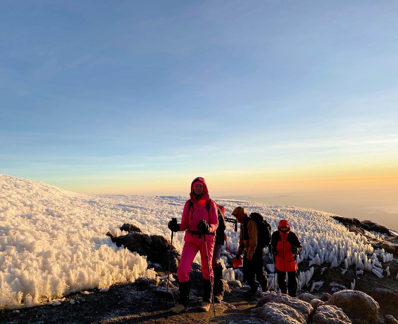 A team of climbers trek towards the snow capped summit of Mount Kilimanjaro as the sun rises behind.