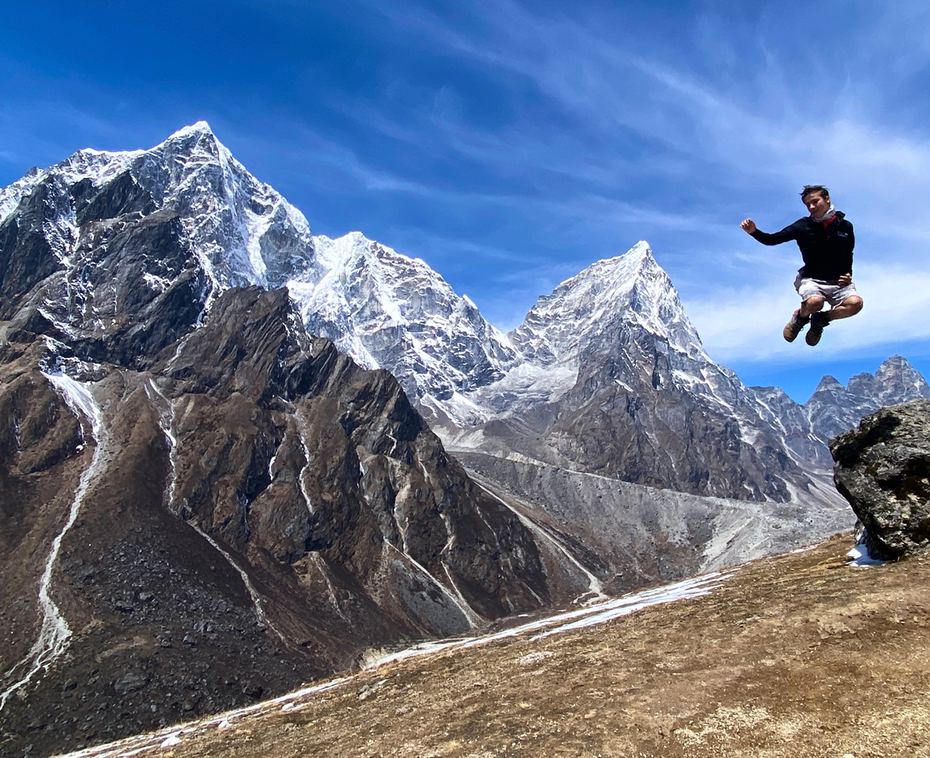 A teenager jumps off a rock enroute to Everest Base Camp with the stunning backdrop of Himalayan peaks Lobuche and Cholatse