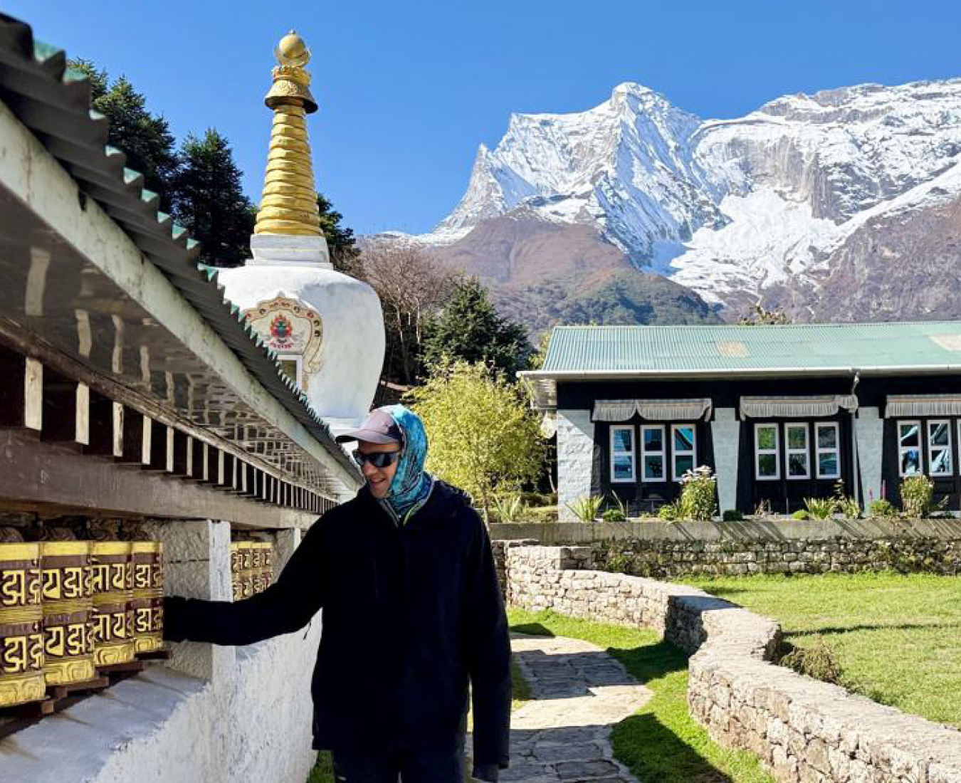A trekker spins prayer wheels in the lower Khumbu Valley near Namche. Snow covered peaks and bright blue sky beyond.