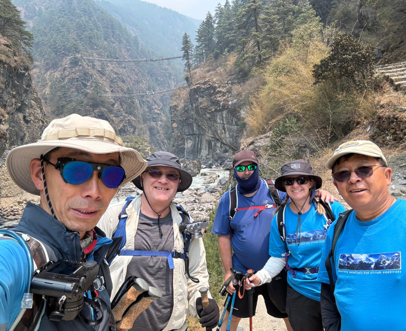 The Three Passes Nepal 2024 #1 Team, stop for a group selfie just before the Namche bridge seen in the hazy distance between tree clad hills.