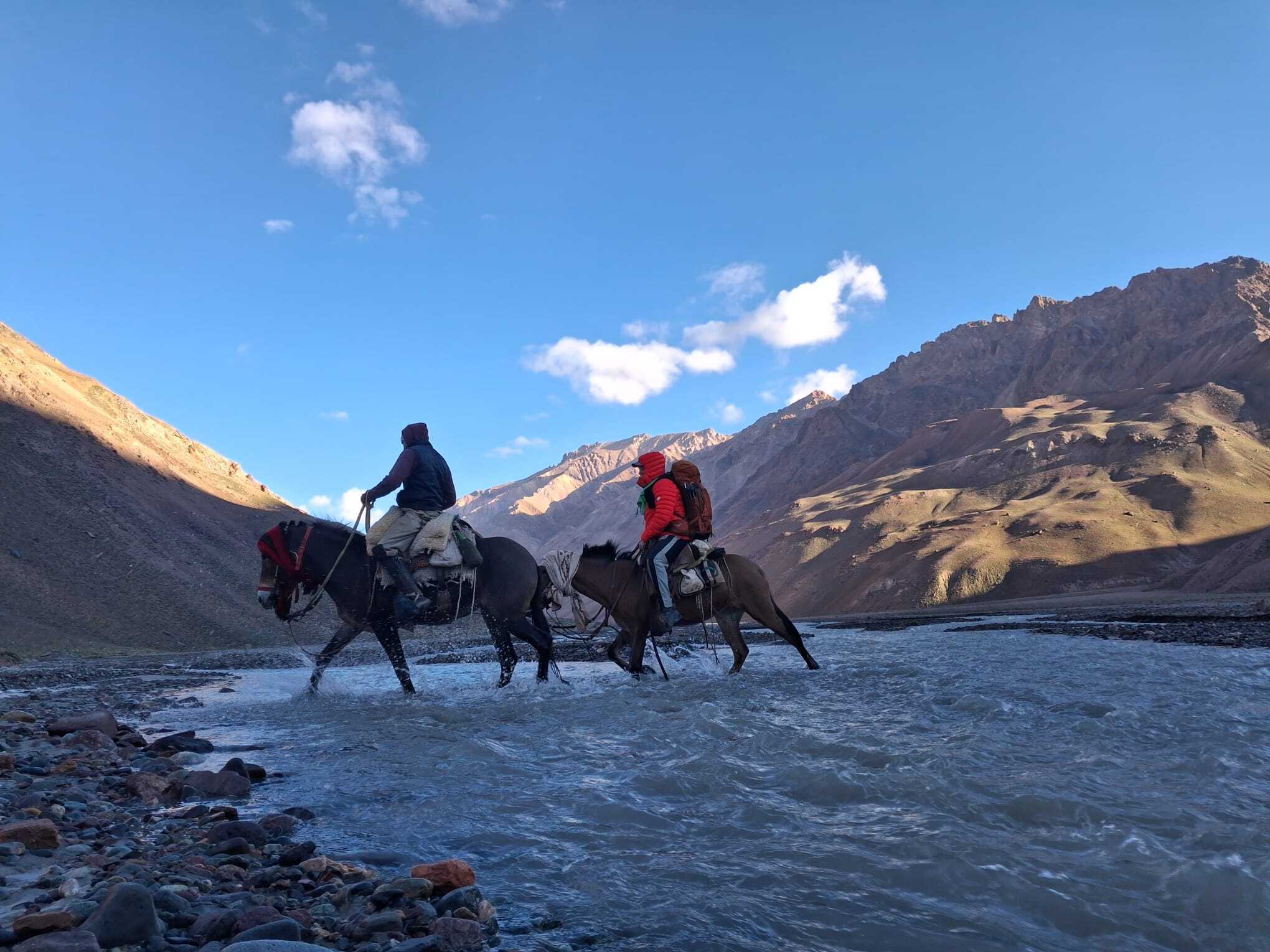 Mule riders crossing a cold mountain river in Vacas Valley on the approach to Aconcagua during a high-altitude expedition.