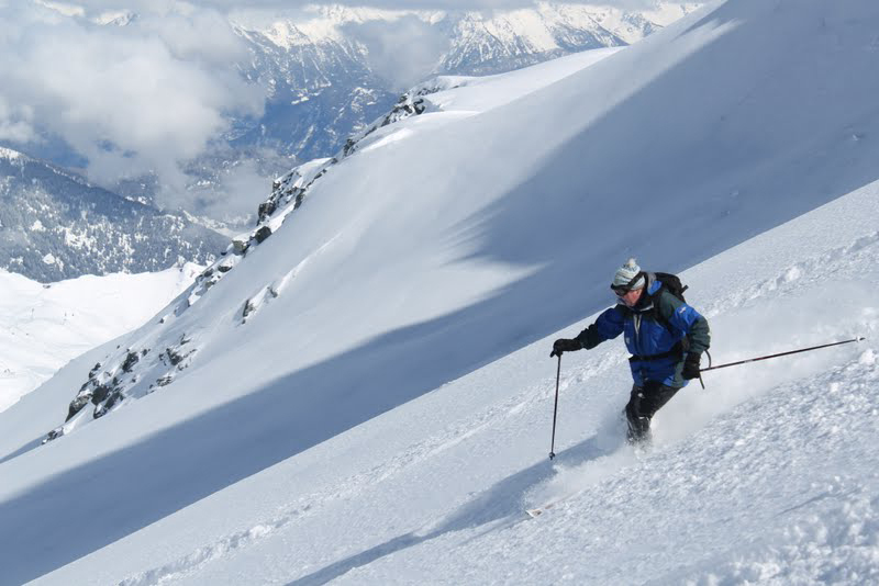 A skier makes fresh tracks on a wide open slope, the vast Swiss Alps in the distance.