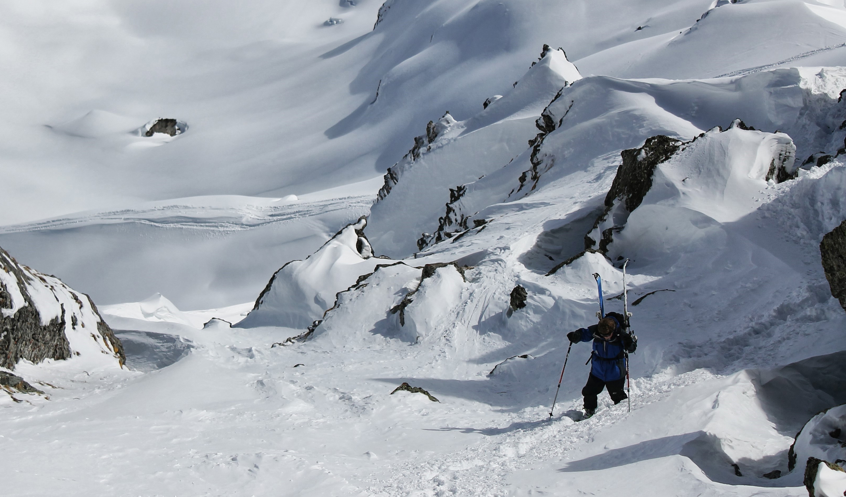 A skier climbs up through challenging terrain, fresh snow coats surrounding rocks.