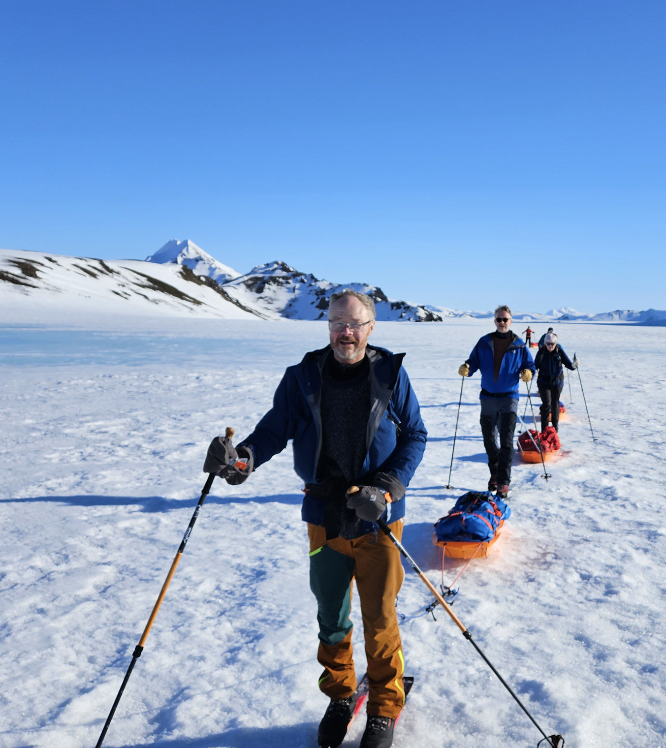 A group of skiers haul sleds with spectacular blue skies and volcanic Icelandic terrain surrounding them.
