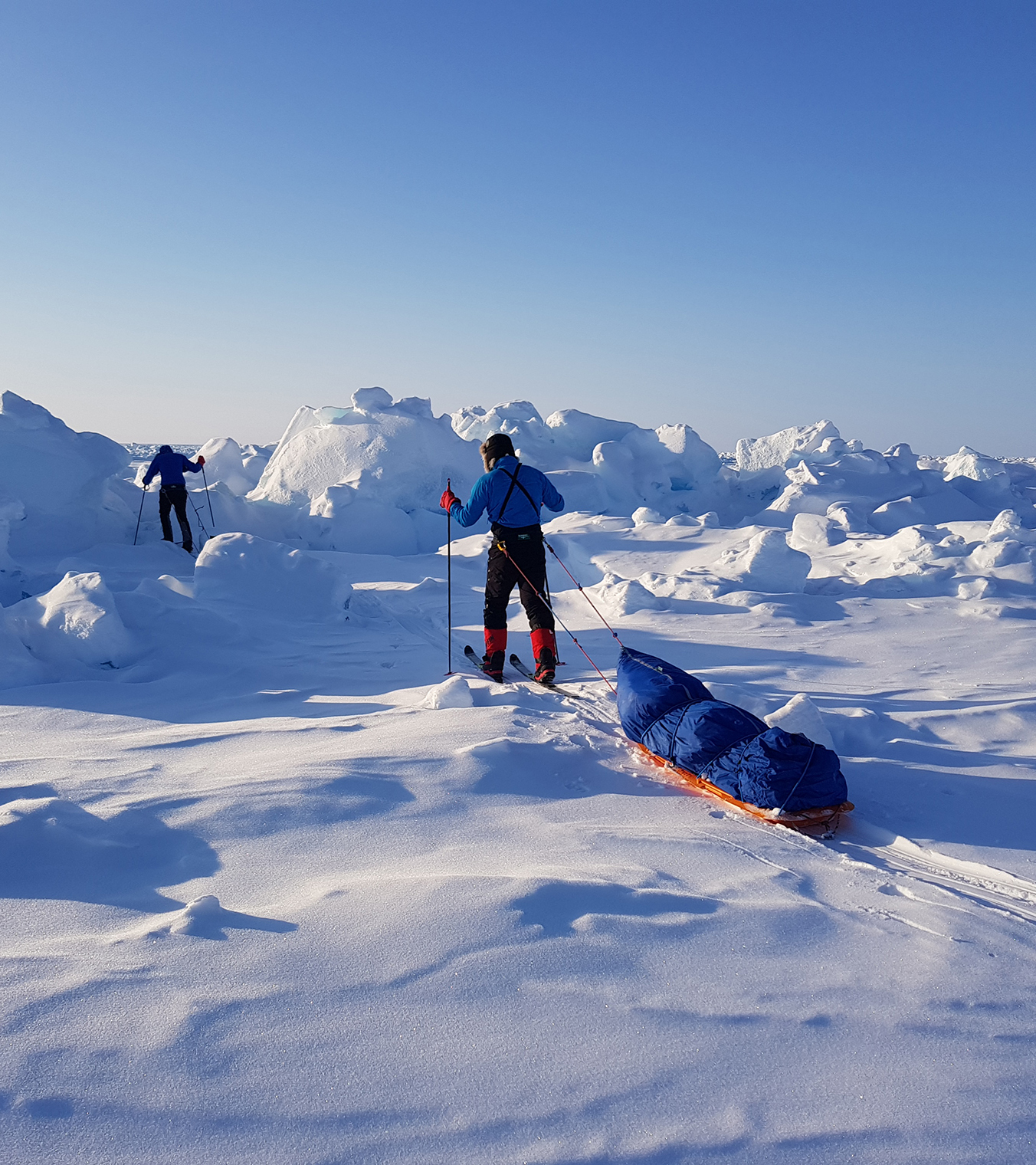 Skiers haul sleds through difficult terrain enroute to the North Pole, in brilliant clear weather conditions.