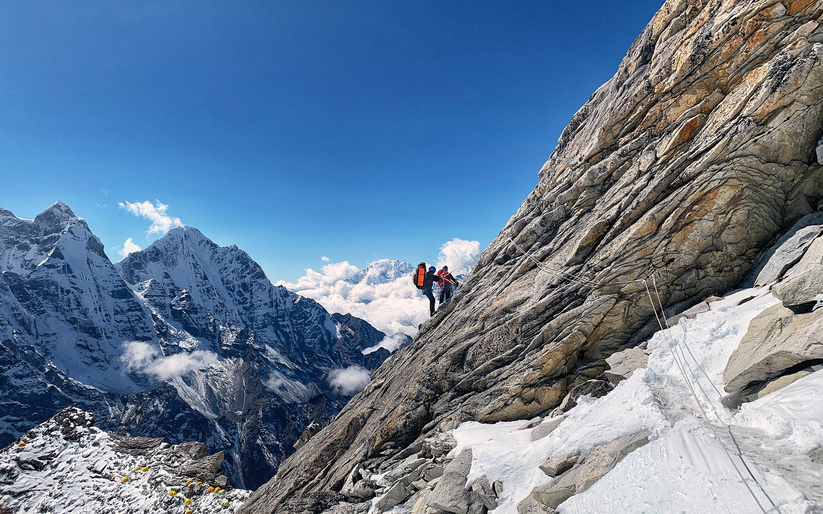 AC IFMGA Mountain & Ski Guide Csomin Andron assists a climber on Mount Ama Dablam, Nepal. Stunning mountain scenery and clouds behind.