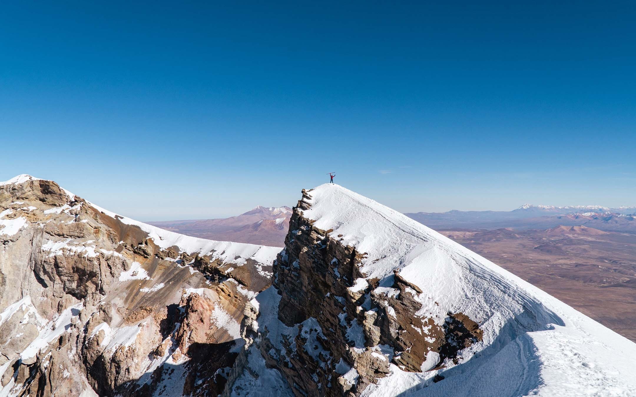 AC IFMGA Mountain & Ski Guide Dave Lewis stands atop of a snow covered mountain dwarfed by the landscape surrounding him.