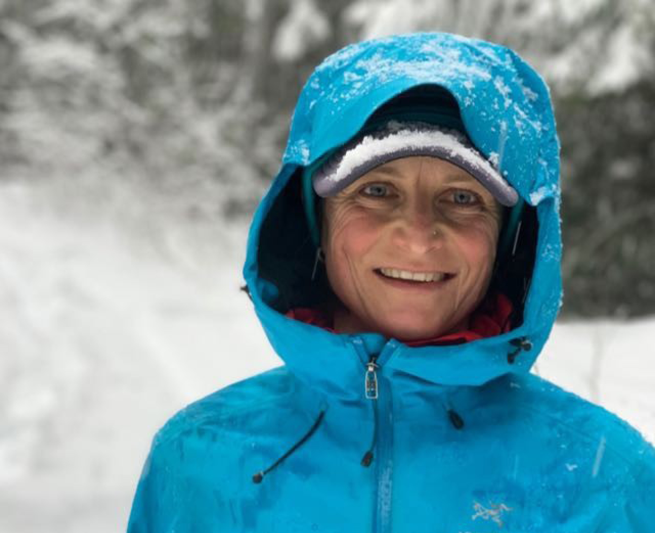 AC Trekking and ACMG Ski Guide Erika Flavelle bright blue rain jacket on and hood up against the elements.