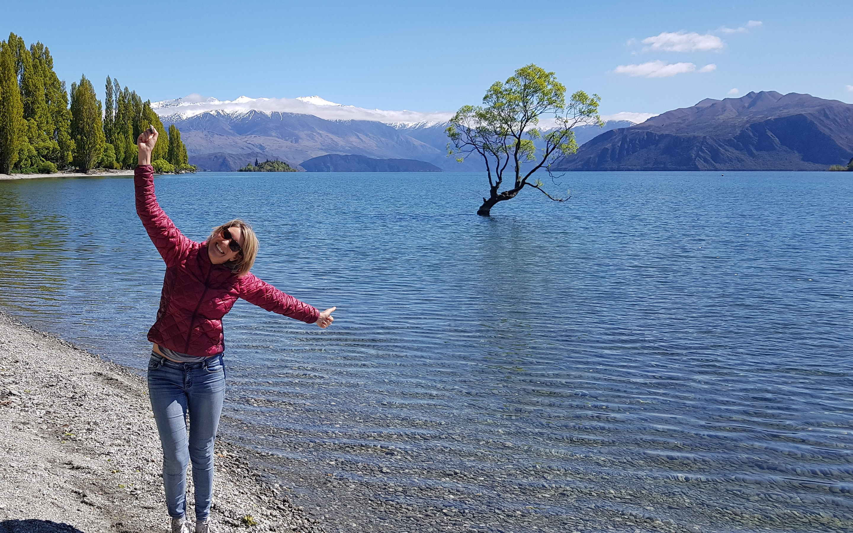 AC Expedition Liaison & Sales team member Jo Clark at 'that Wanaka tree', a willow growing in the middle of Lake Wanaka, New Zealand with spectacular mountain views behind.