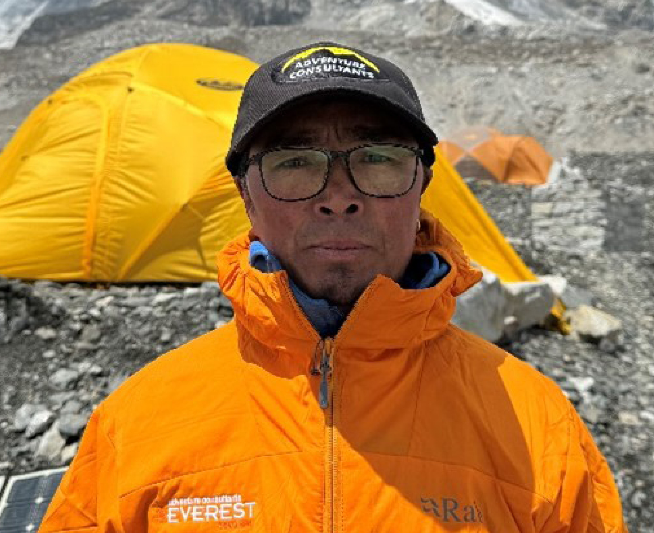 AC Climbing Sidar Chhewang Dorji Sherpa at Everest Base Camp with a tent and glacial rock behind