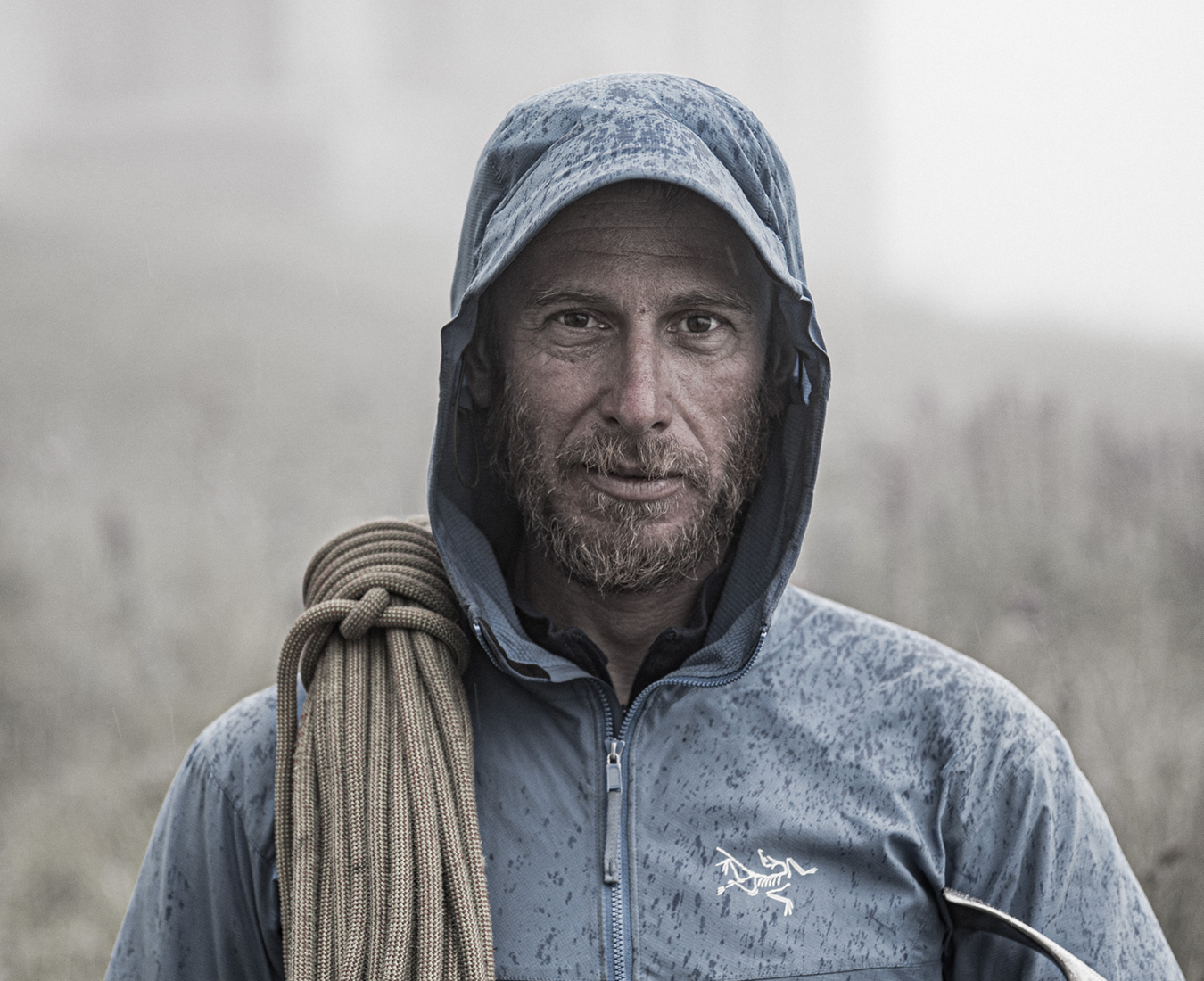 Adventure Consultants IFMGA Mountain & Ski Guide Bastian Speckle with hood on in the rain and a rope over one shoulder.