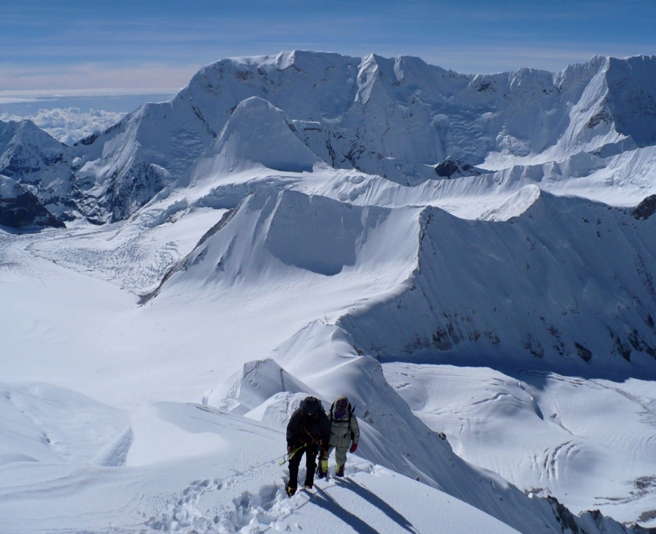 Climbers high on the snow covered South Ridge of Baruntse, views across the Himalaya stretch out behind them.