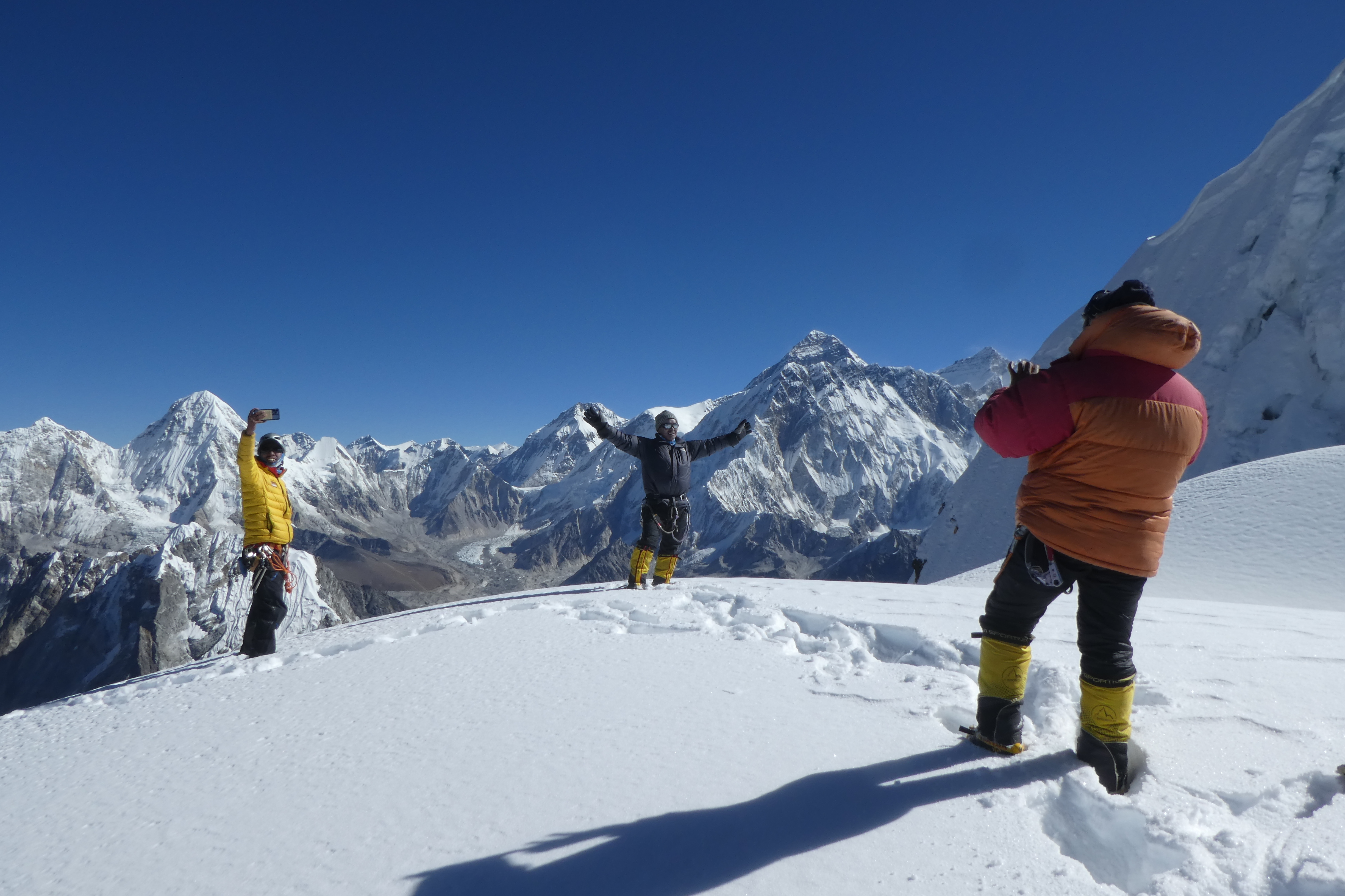 A team take photos looking towards Everest from the summit of Cholatse