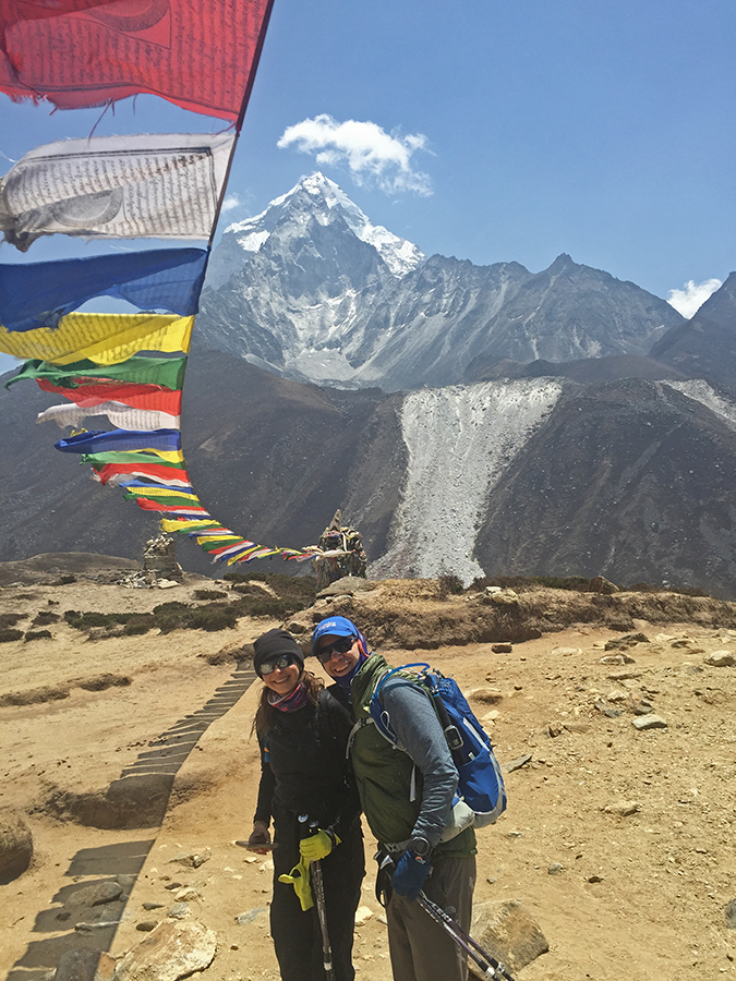 Trekkers stand in front of Ama Dablam, the jewel of the Khumbu Valley. Prayer flags wave above.
