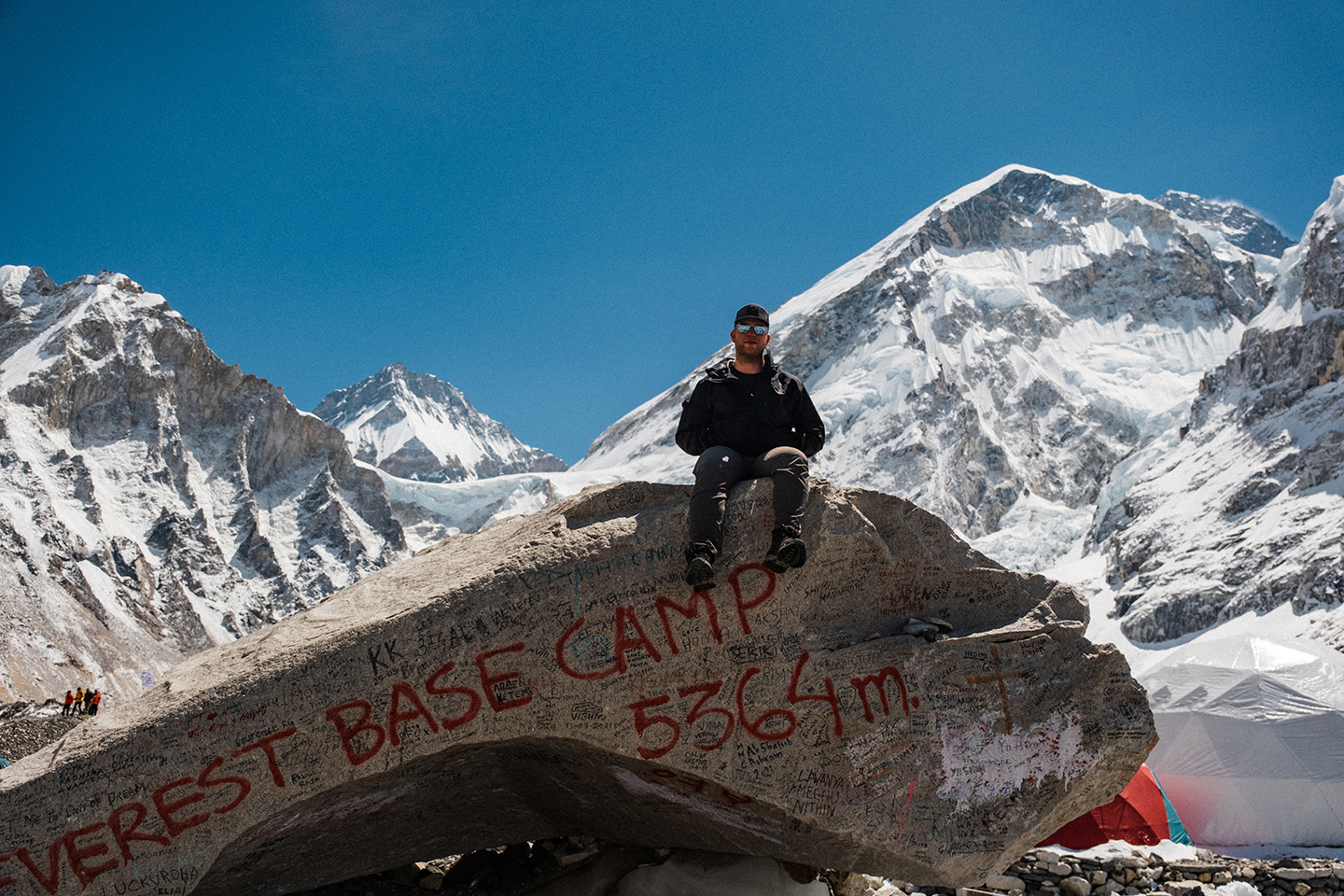 A trekker sits on the famous 'Trekkers Rock' which marks the entrance to Everest Base Camp, the West Shoulder of Mount Everest standing tall in the background.