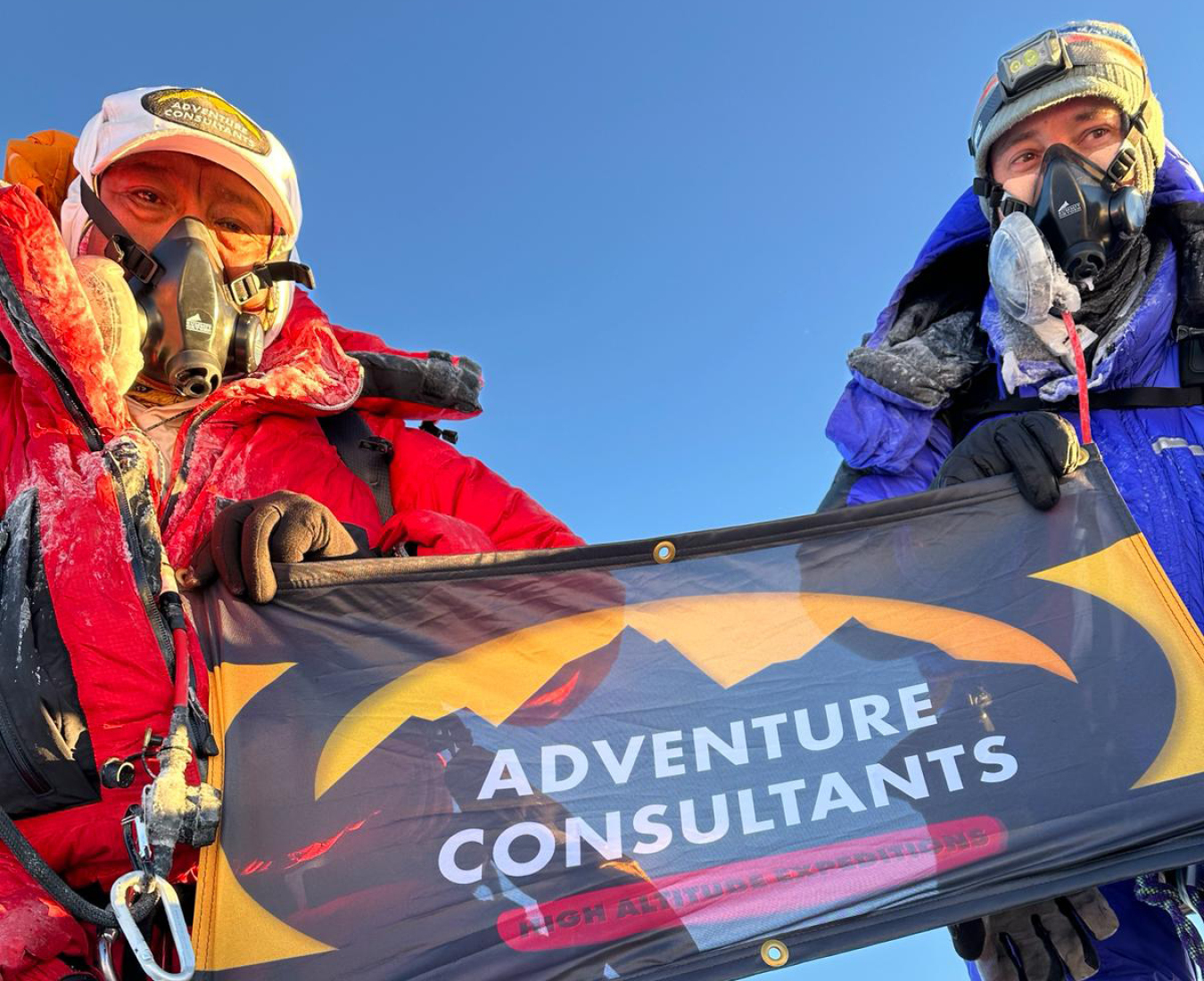 AC Guide Ang Dorjee Sherpa and a fellow climber stand on the summit of Mount Everest proudly displaying an Adventure Consultants flag.