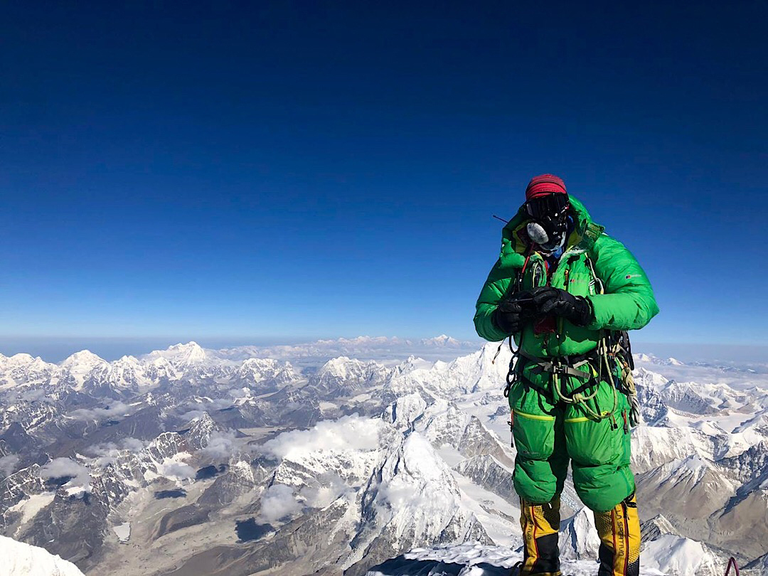 Climber in green suit on summit of Mt Everest