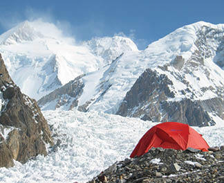 A bright red tent pitched on glacial moraine with the Baltoro Glacier and Gasherbrum peaks behind