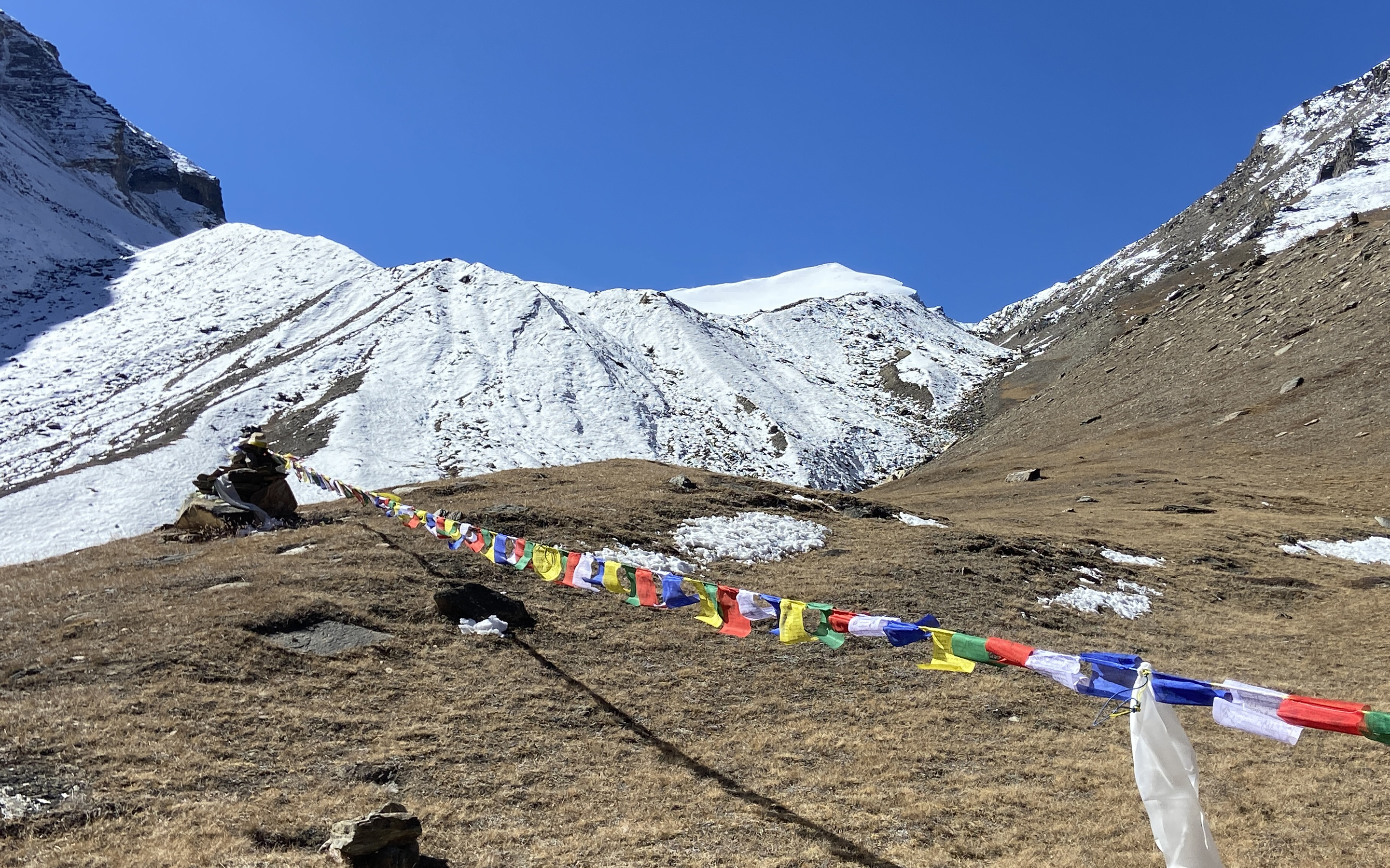 Prayer flags wave in the breeze from a chorten near base camp on Putha Hiunchuli in front of a large glacier.