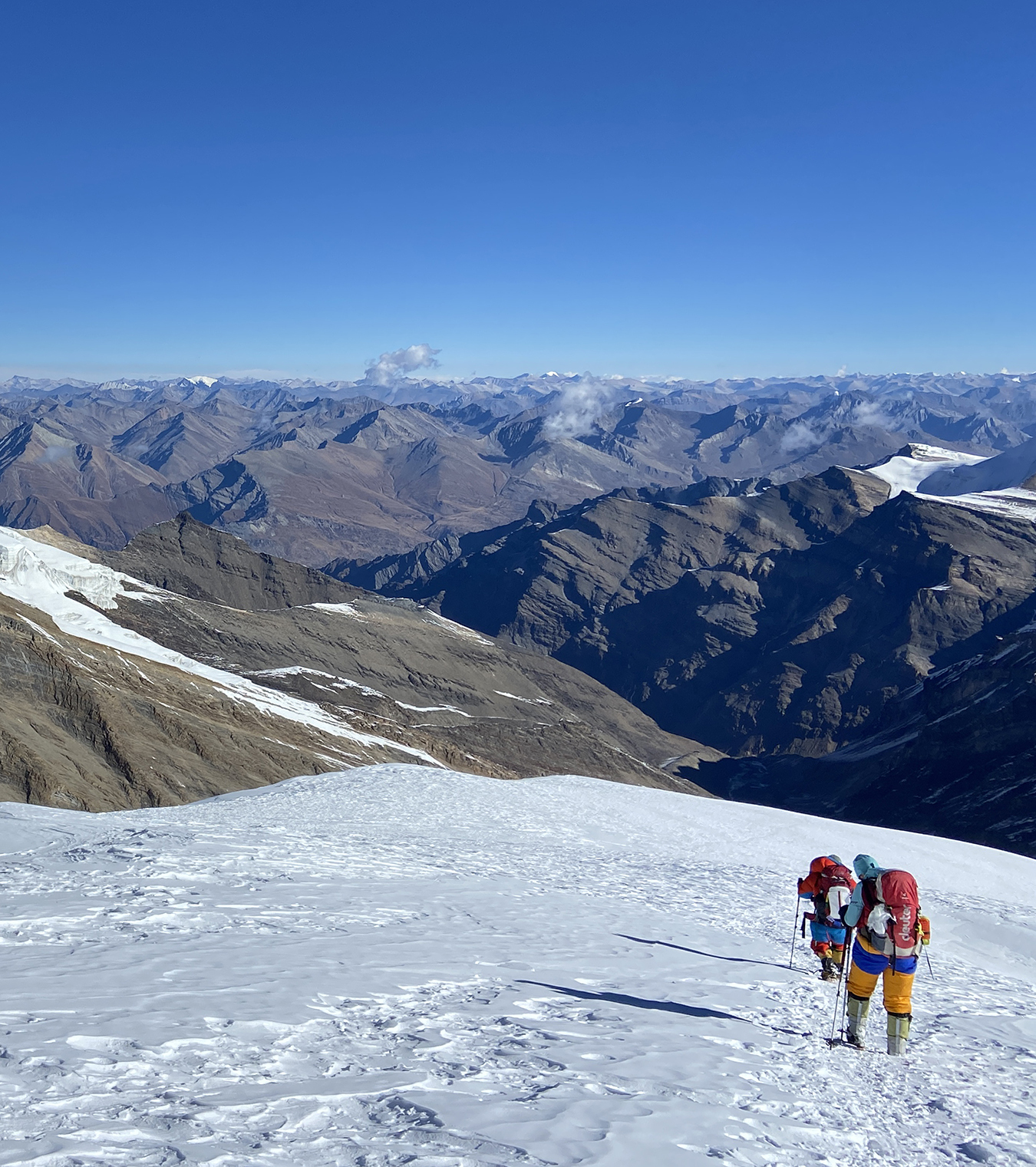 Two climbers descend the snow slopes of Putha Hiunchuli, with views extending out across the Doplo area of Nepal to a distant mountainous horizon.