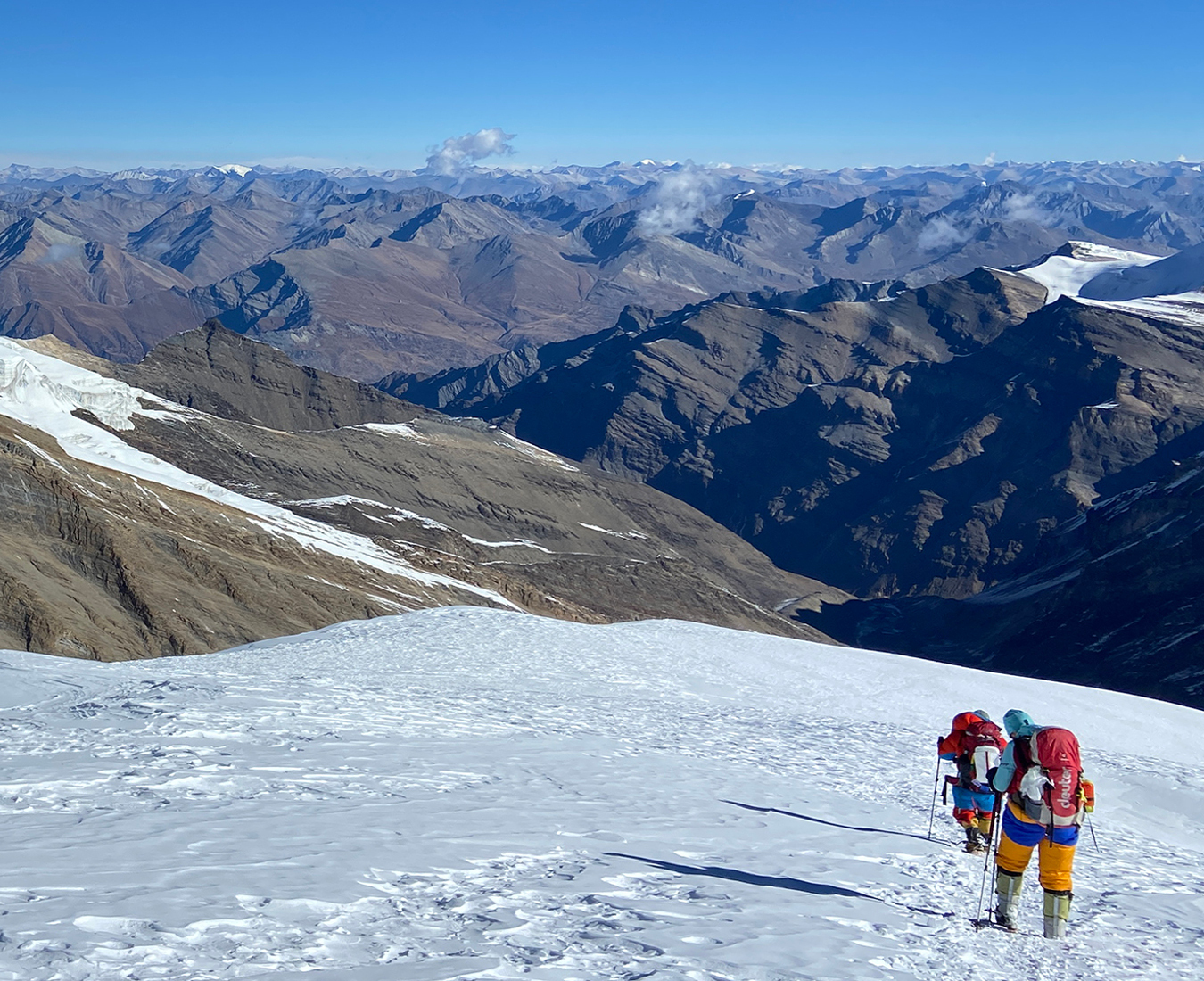 Two climbers descend the snow slopes of Putha Hiunchuli, with views extending out across the Doplo area of Nepal to a distant mountainous horizon.