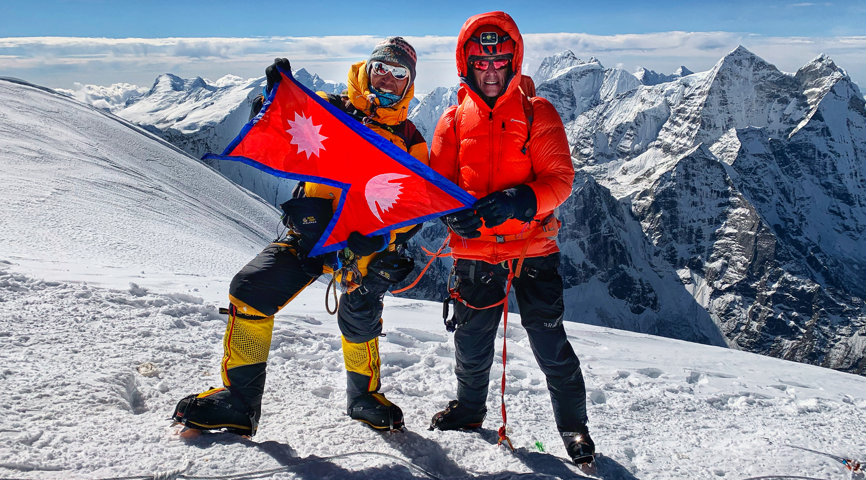A climber and Sherpa wave the Nepalese Flag from the summit of Mount Ama Dablam.