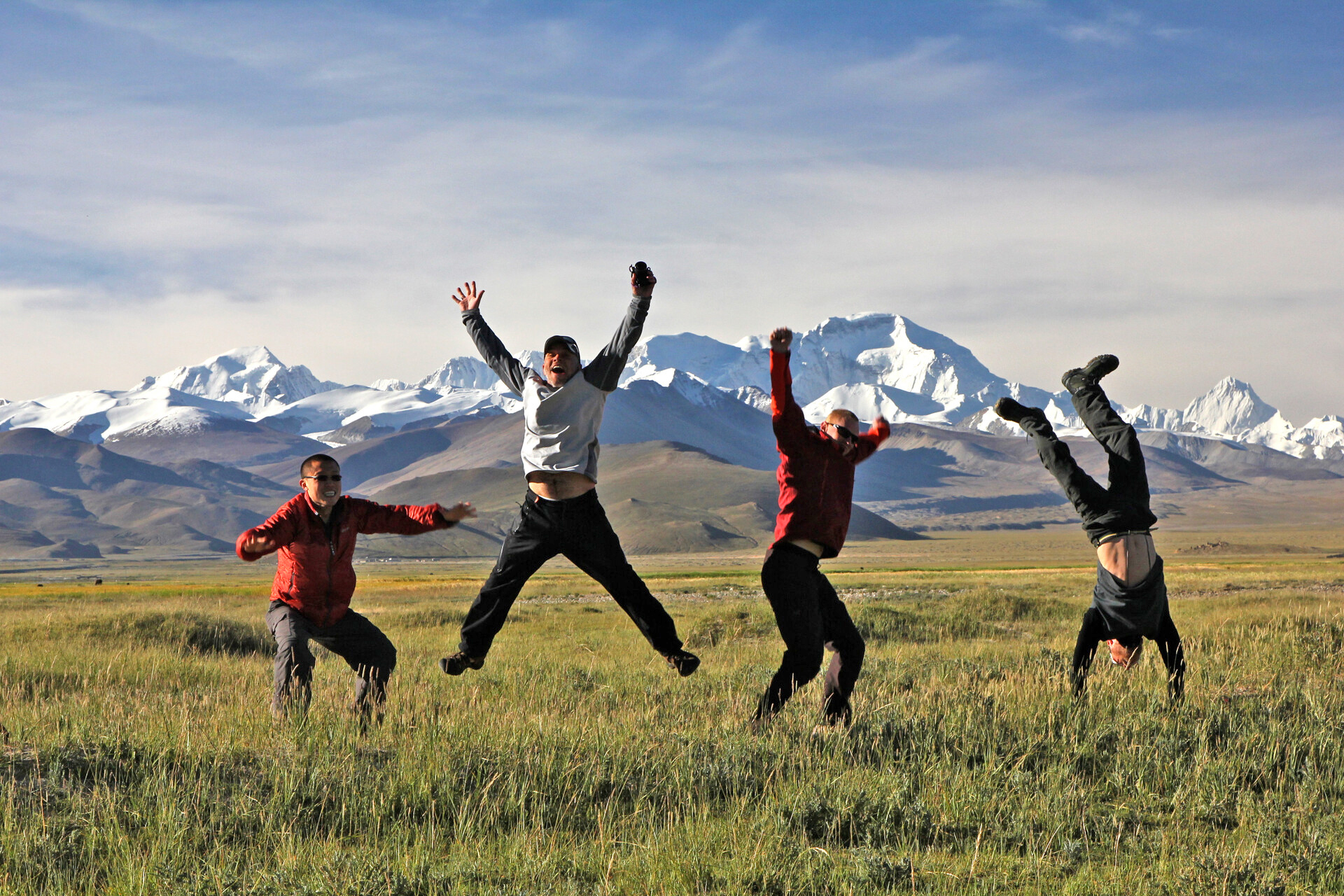 A group jumping with excitement as they cross the Tibetan plateau, a snow capped Mount Cho Oyu in the distance.