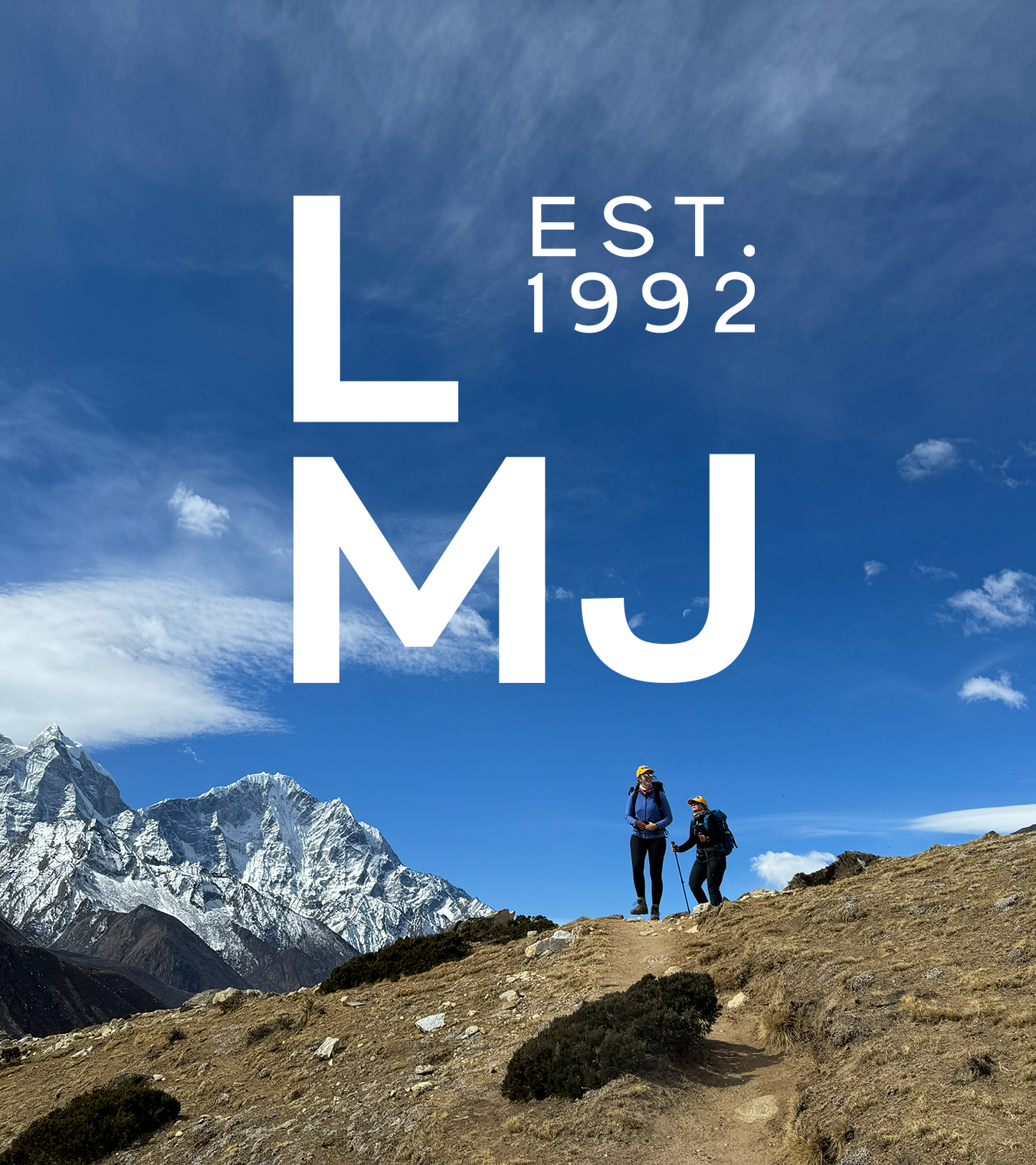 Luxury Mountain Journey logo overlays an image of two trekkers dwarfed by the mountainous terrain around them and big, bright blue sky above.