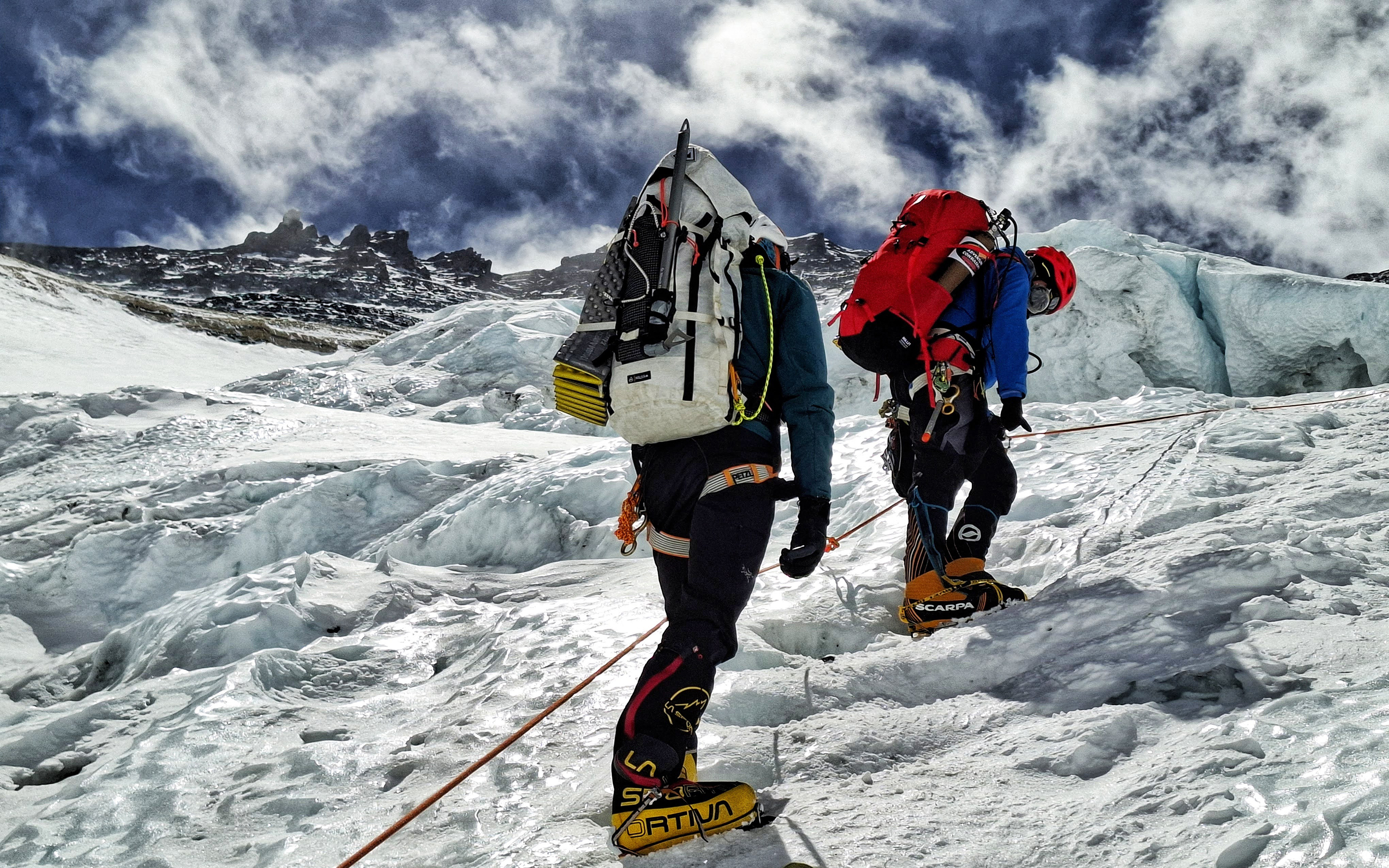 two climbers, packs laden with gear and oxygen ascend fixed lines on Everest with towering peaks above them. Photo by AC Guide JB Chandesris.