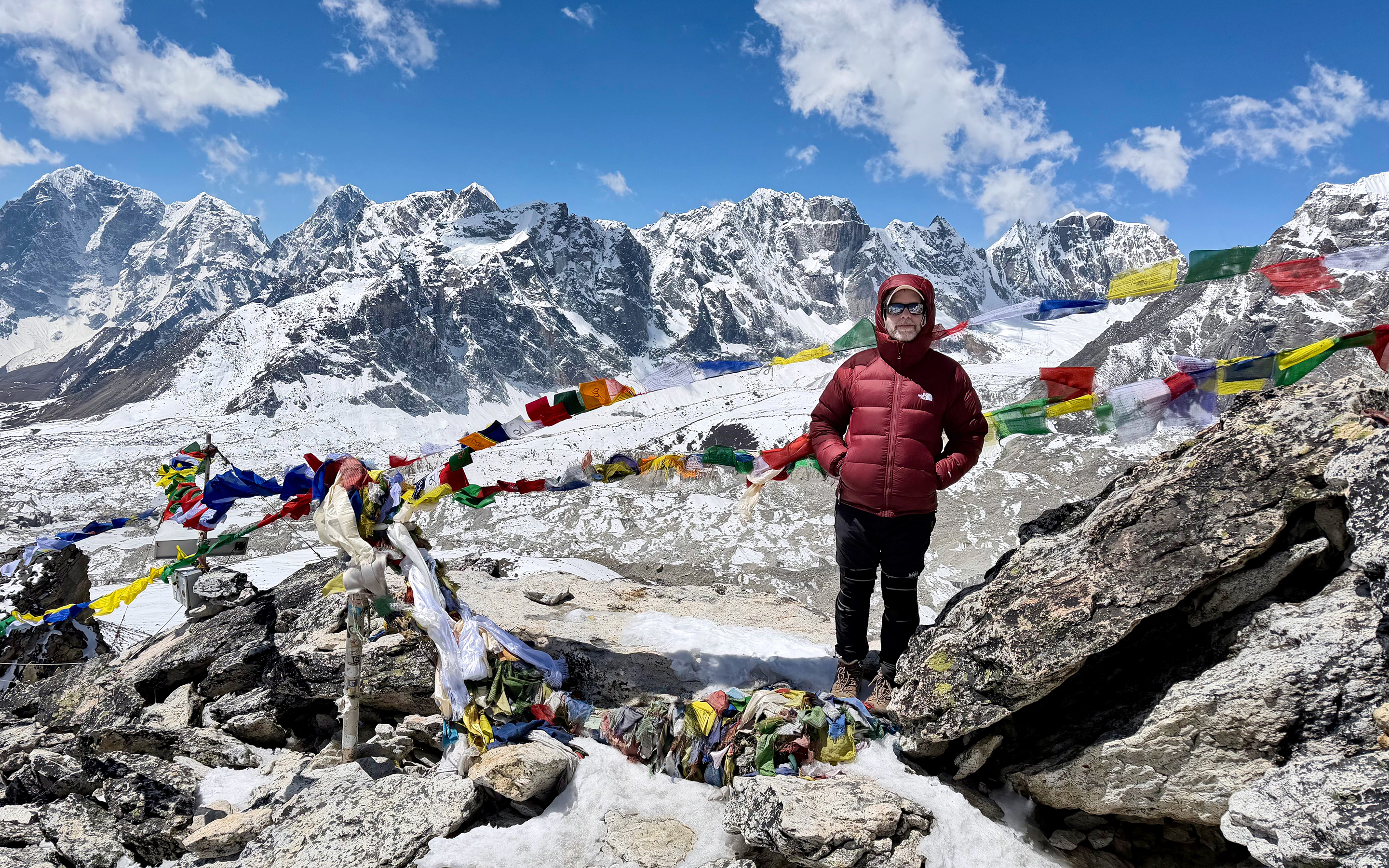 A trekker stands on Kala Patar and soaks in the fabulous surrounding mountain views with prayer flags fapping in the wind.