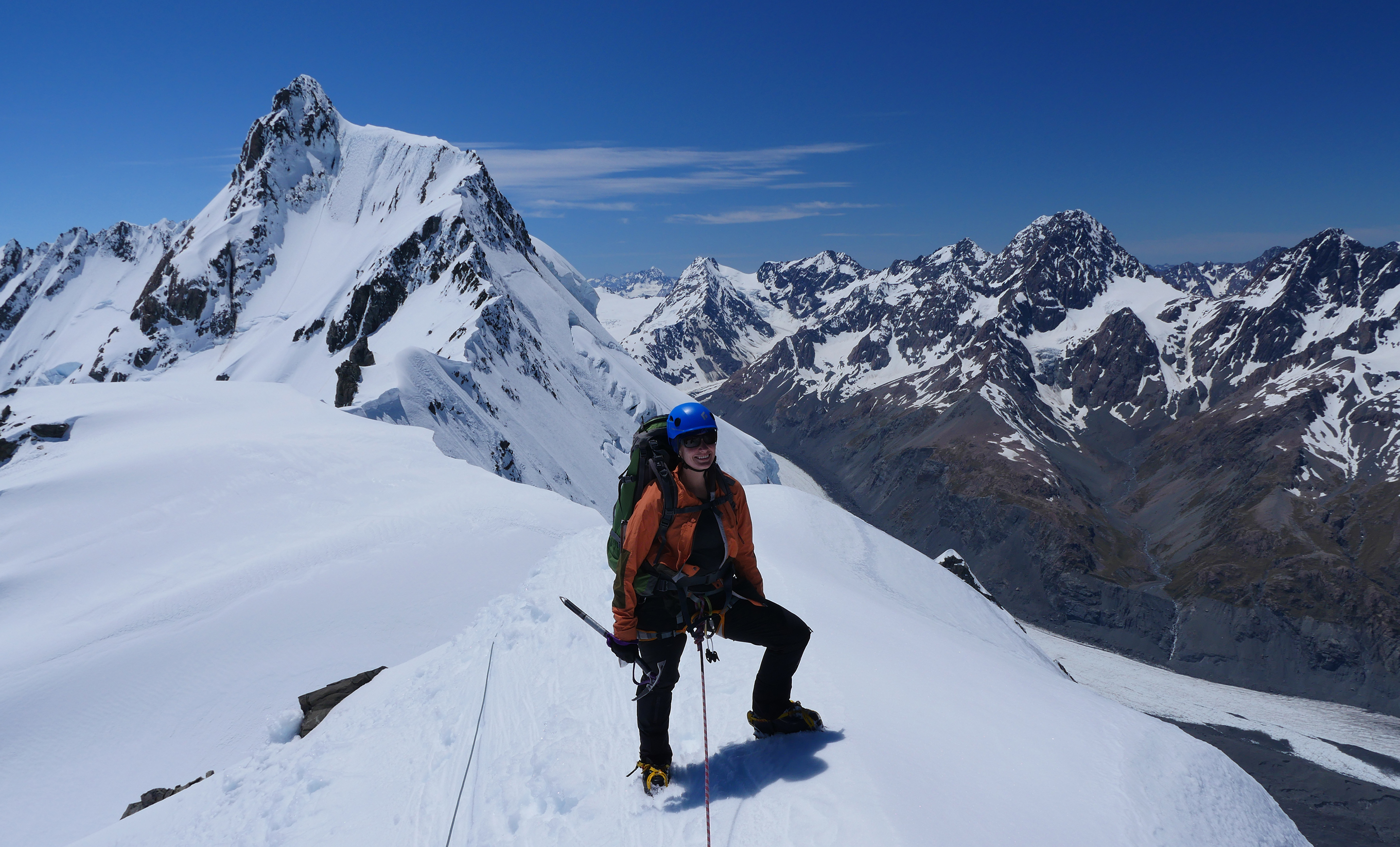 A climber on an introductory mountaineering course stands on the spine of the Southern Alps, the Tasman Glacier can be seen far below.