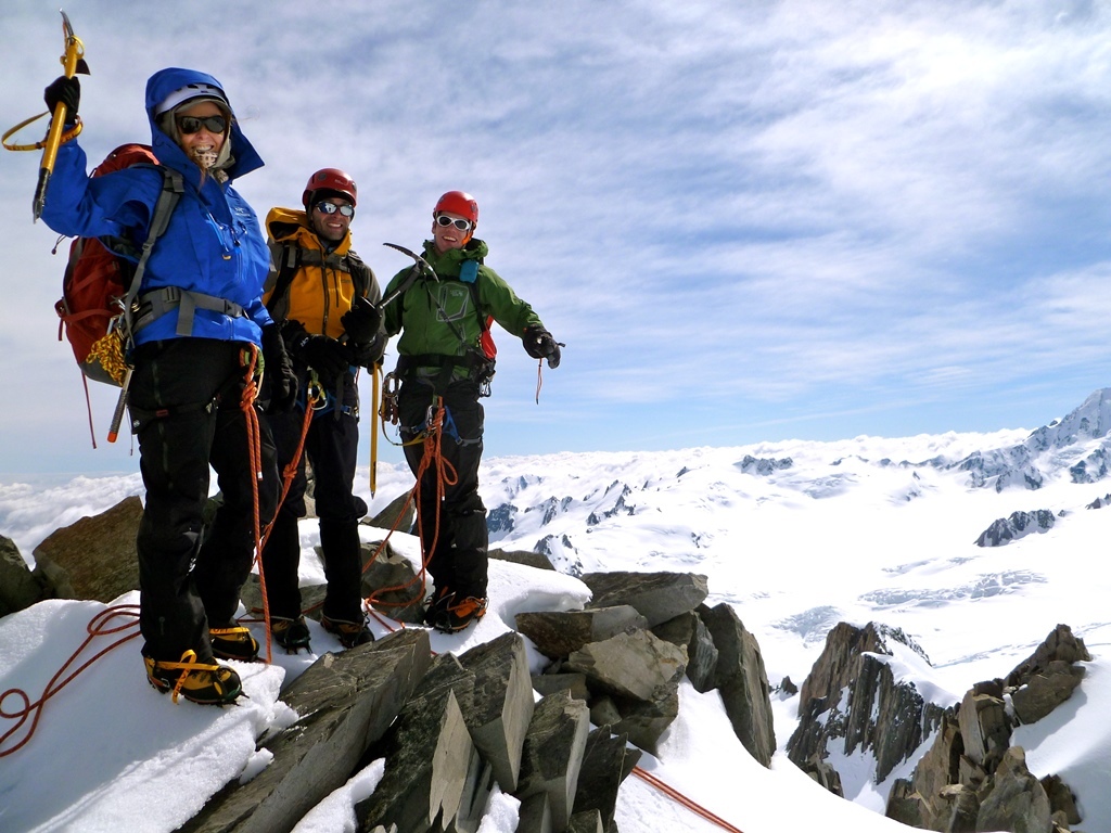 A team of climbers summit a peak in New Zealand's Southern Alps, cloud obscures the scenery below.