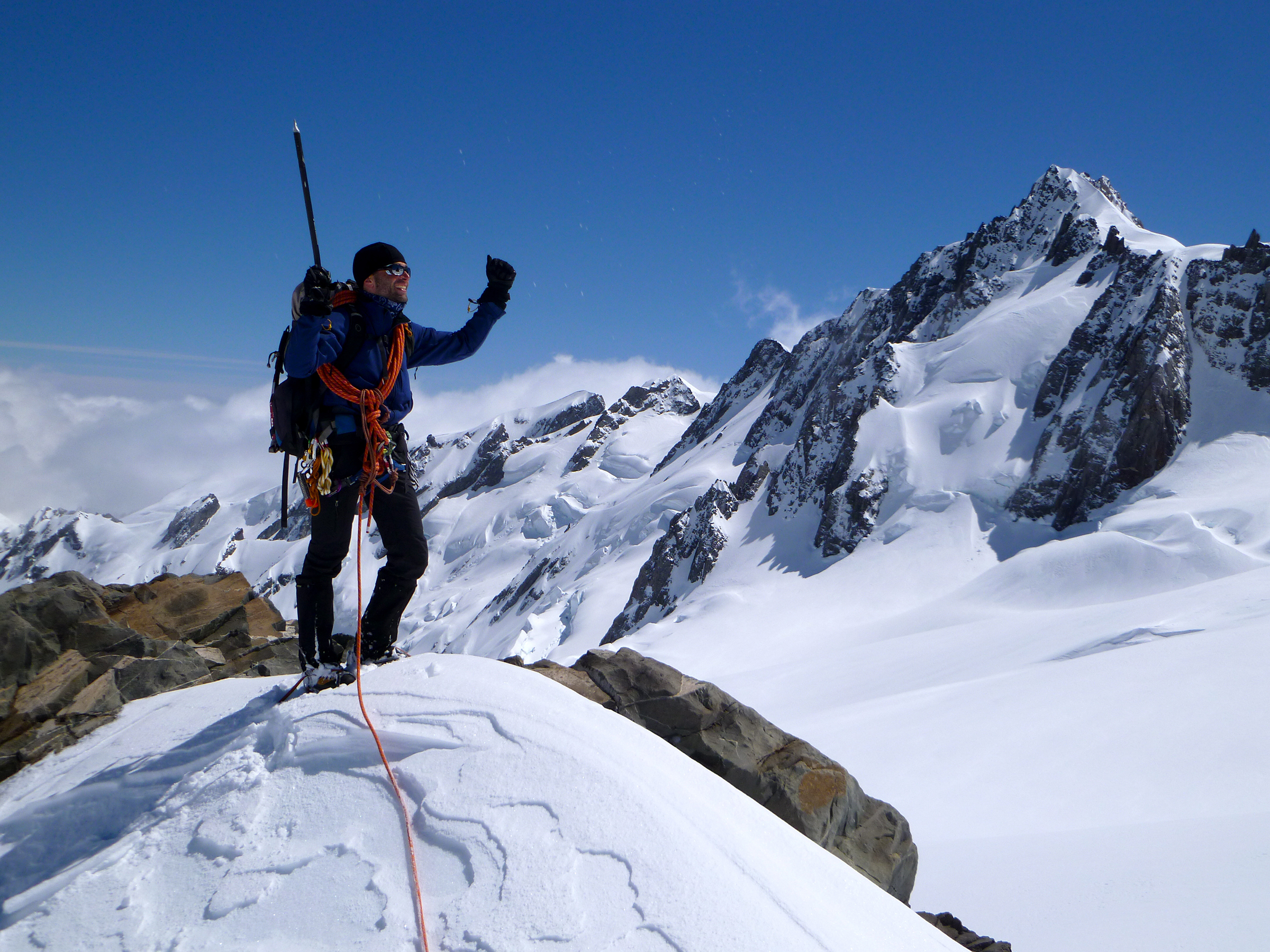 A climber fist pumps triumphant on their successful summit, New Zealand.