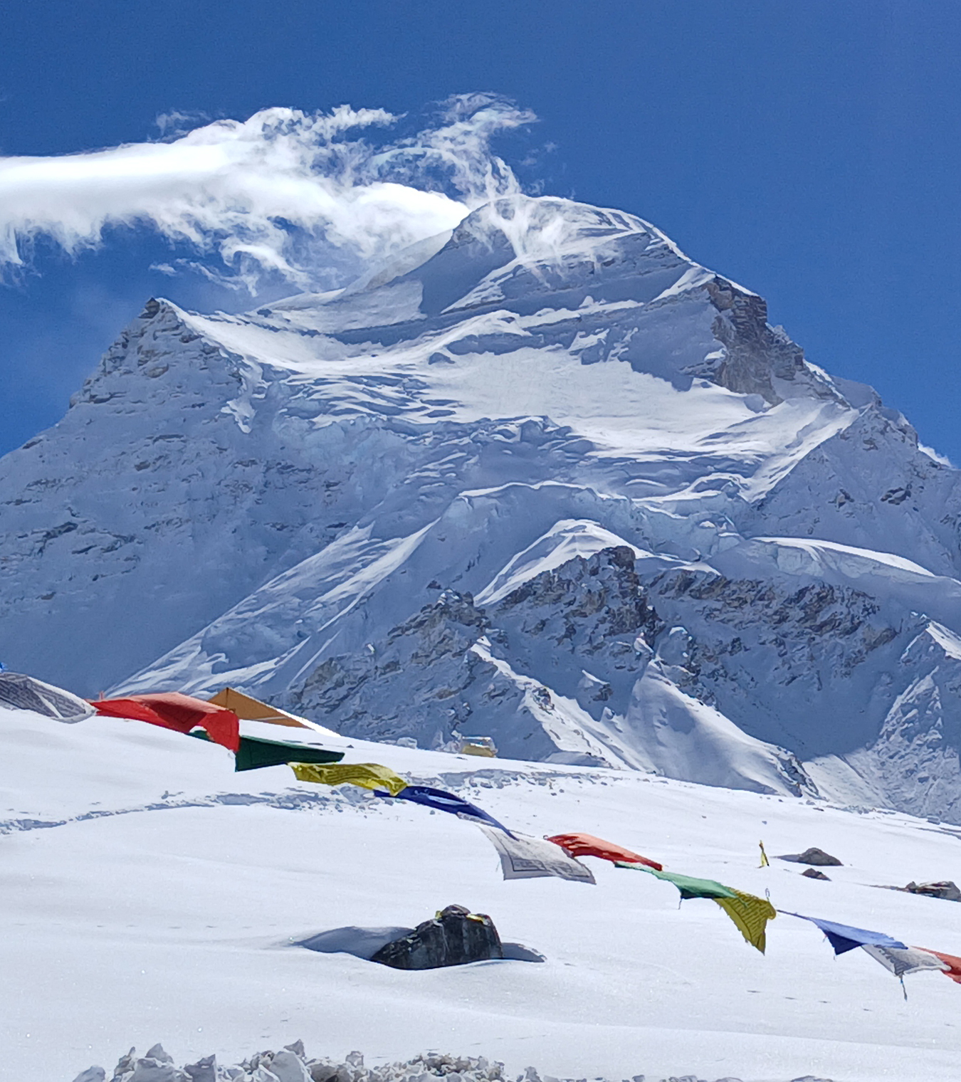 Cho Oyu, partly obscured by cloud looks magnificent from Base Camp with fresh snow all around. Prayer flags wave in the wind nearby