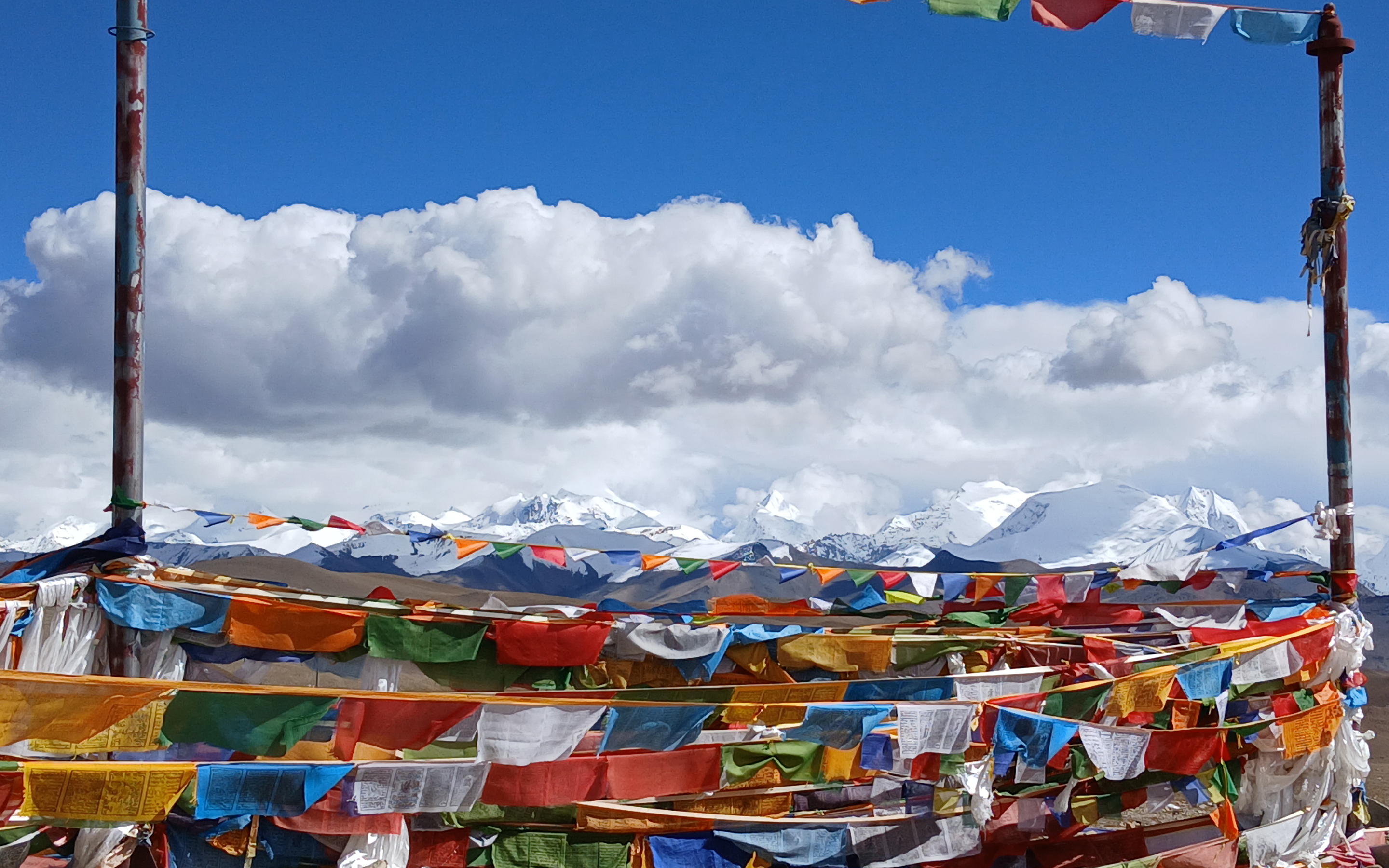 Prayer flags adorn a high pass enroute across the Tibetan plateau to Cho Oyu. Distant mountains obscured by cloud but blue sky above.