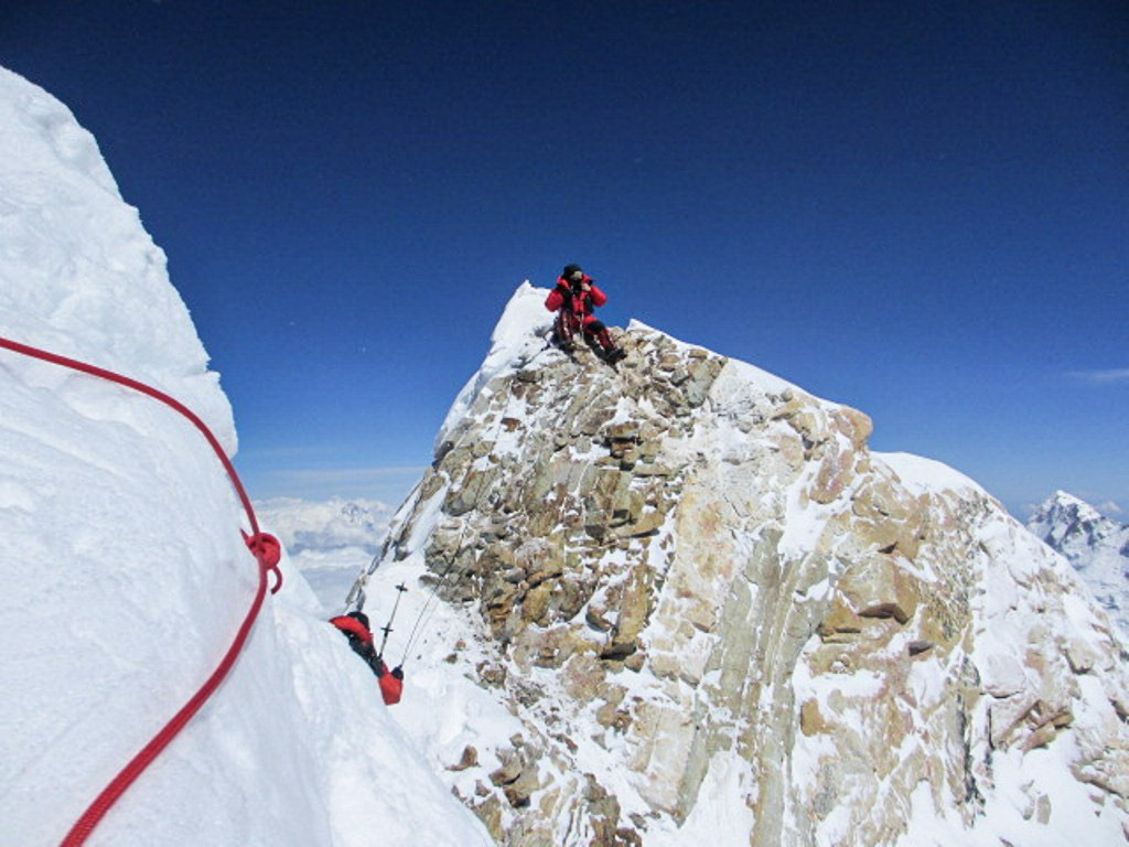 Donal balances on Manaslu’s true summit, clipped to fixed ropes as steep snow and rock fall away on all sides