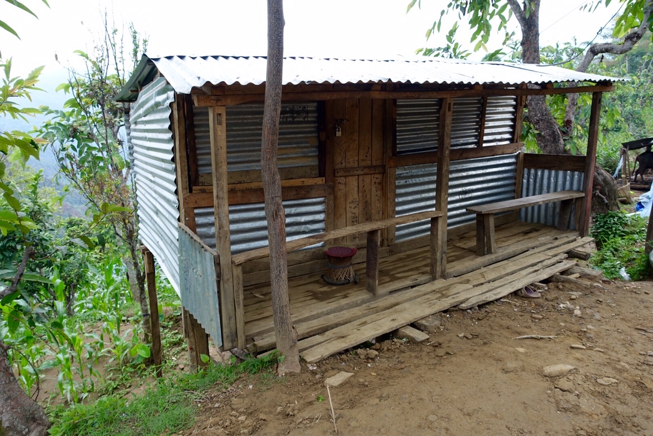 Oxfam relief tents stand on a muddy hillside in Gorkha, Nepal, showing a temporary humanitarian camp set among trees and mountain villages